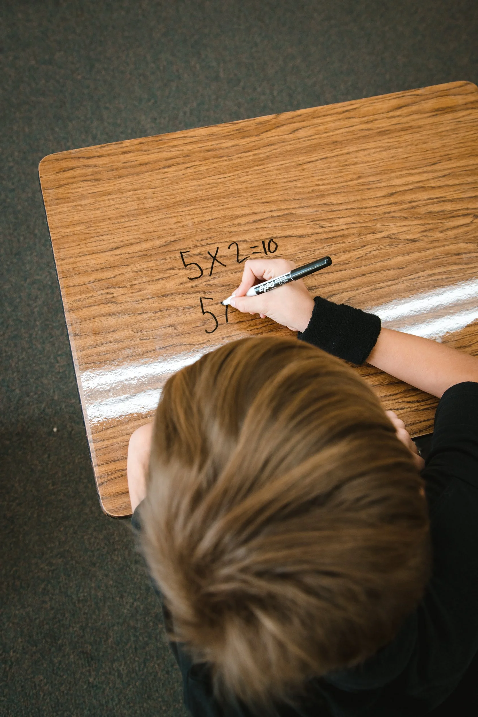 Overhead view of a student adding math equations to a clear dry erase desk wrap.