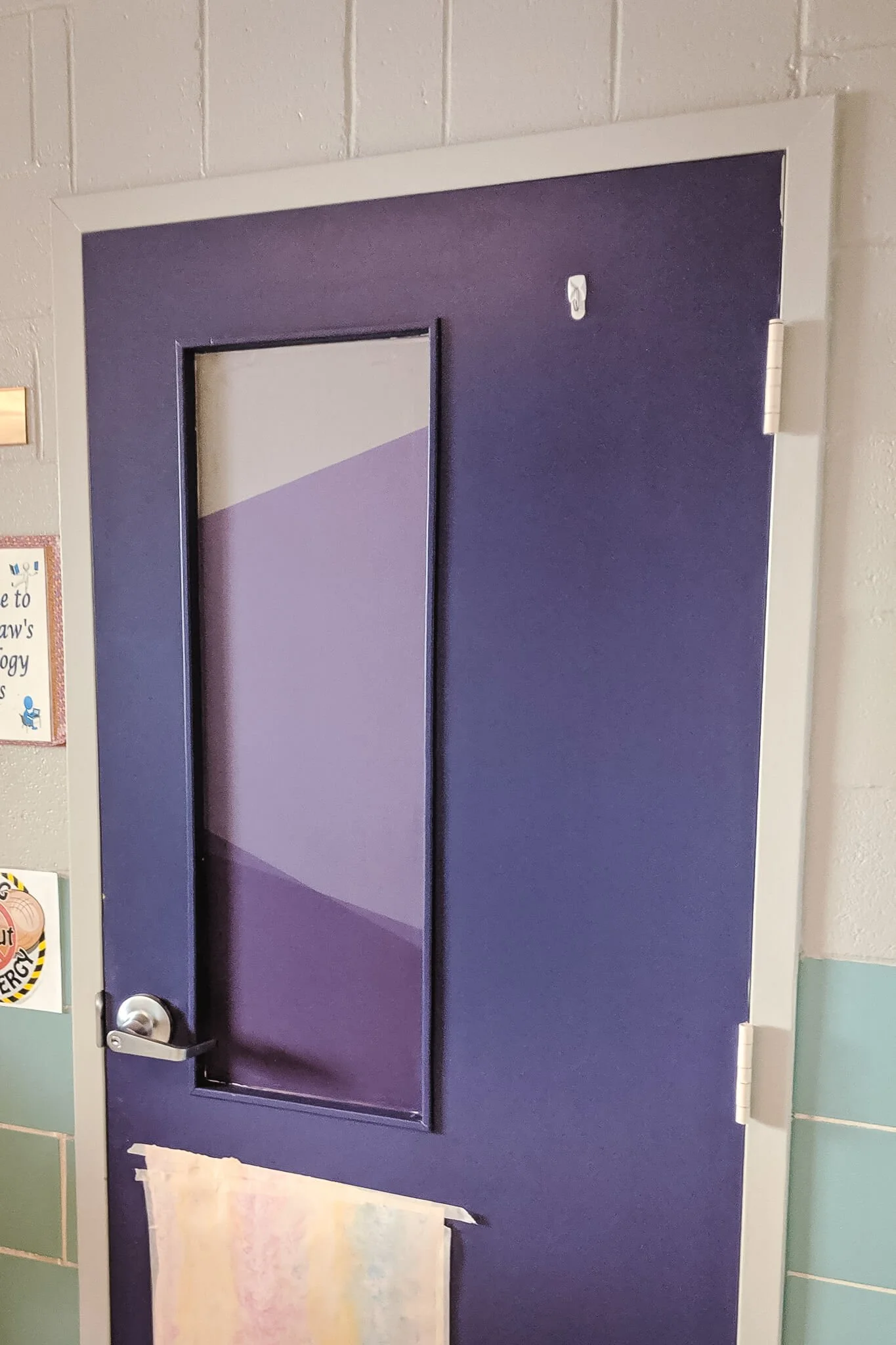 An interior institutional door with a narrow vertical window featuring geometric frosted window graphics in layered purple tones for privacy and visual interest.