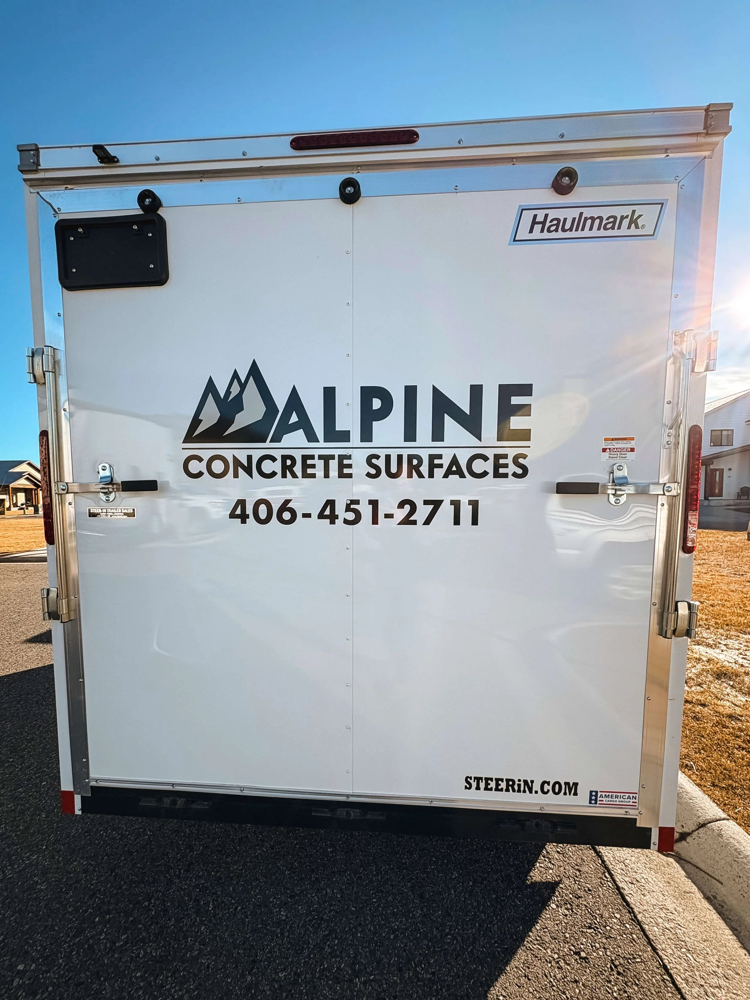 Rear view of a white trailer with a graphic of a mountain next to simple Alpine Concrete Surfaces text