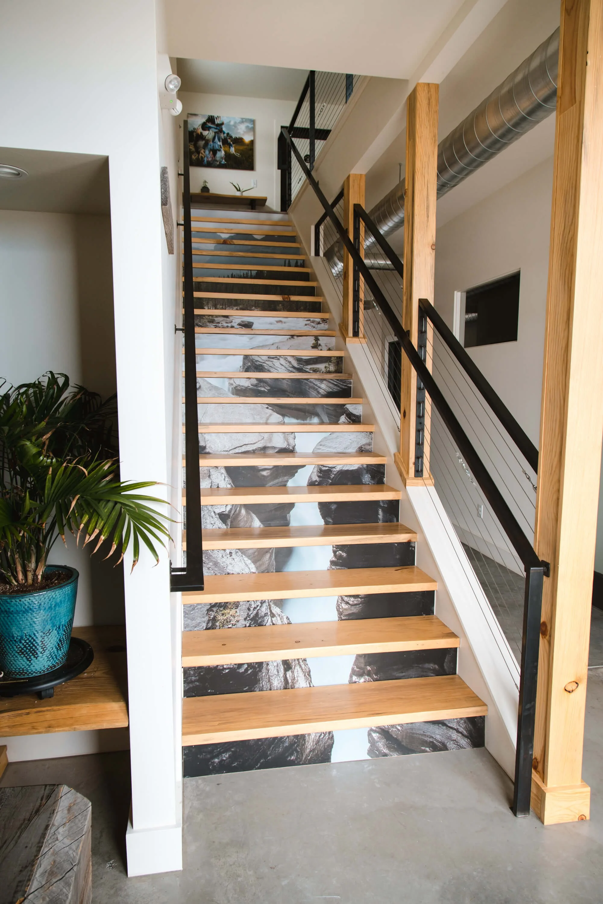 Custom vinyl wraps installed on stair risers, creating a continuous mountain landscape image as part of an indoor branding or design enhancement.