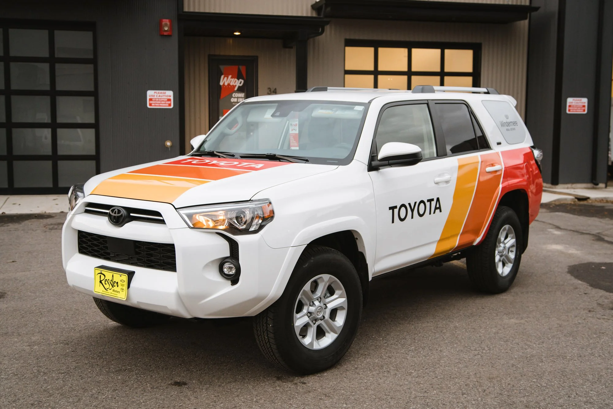 Toyota SUV wrapped in gradient orange, yellow, and red stripes over white with clean black Toyota branding; a fleet wrap designed for high brand visibility and modern style in Bozeman, Montana.