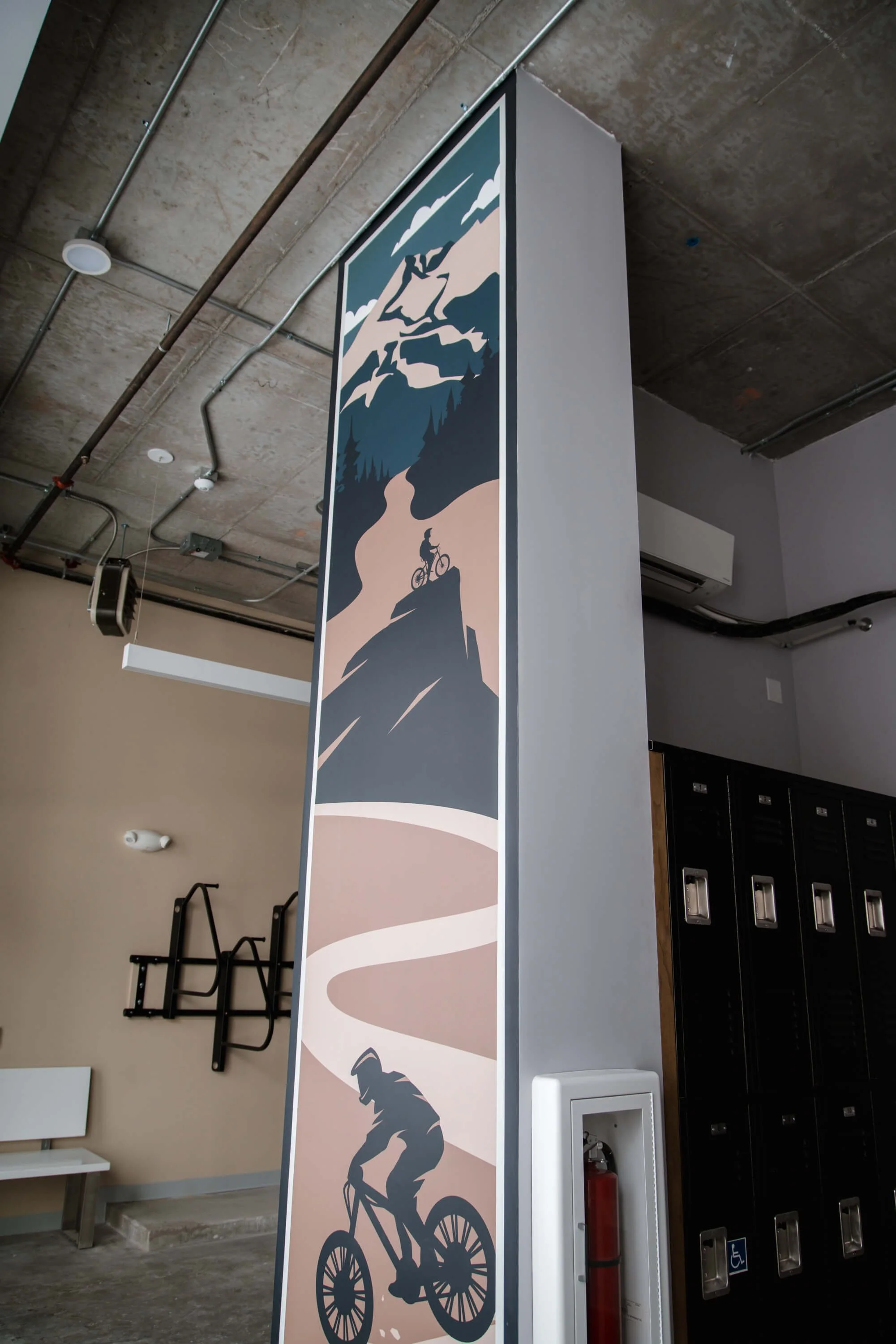 Vertical wall wrap on a structural column featuring minimalist illustration of mountain biking on a winding trail with mountains in the background. Installed by The Wrap Agency at Ives Building.