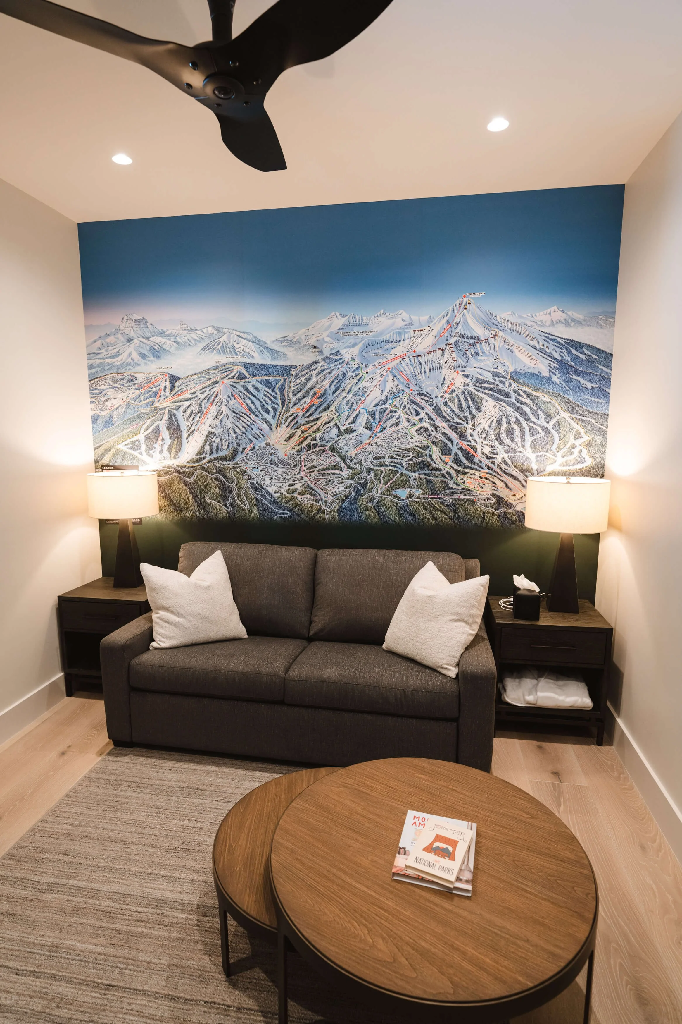 Modern lounge area with a dramatic ski resort trail map wall wrap covering the wall above a gray sofa with white pillows. Location: Big Sky, MT.