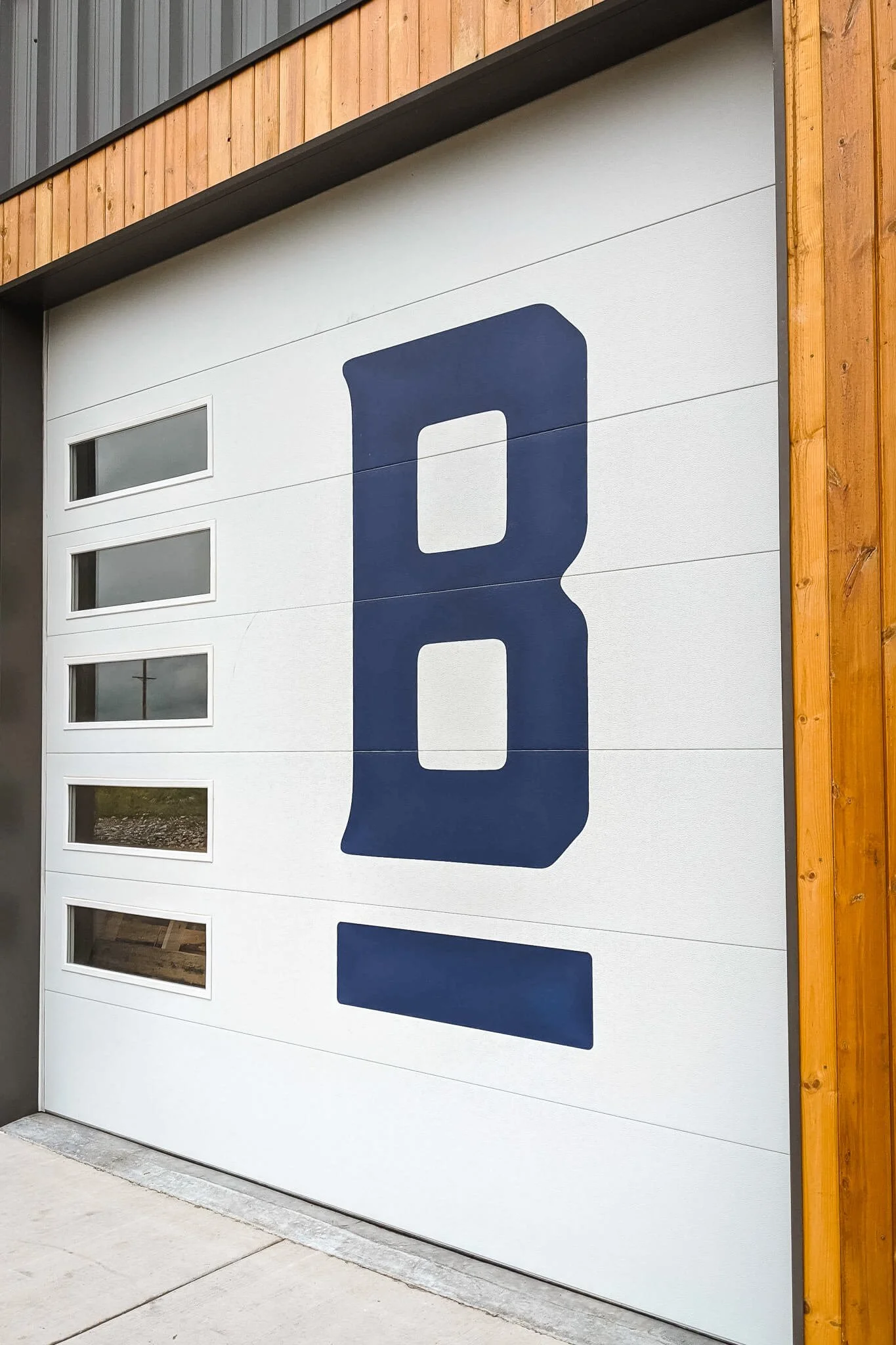 Commercial garage door featuring a minimalist custom vinyl wrap design with a bold navy blue letter “B” and clean white background.