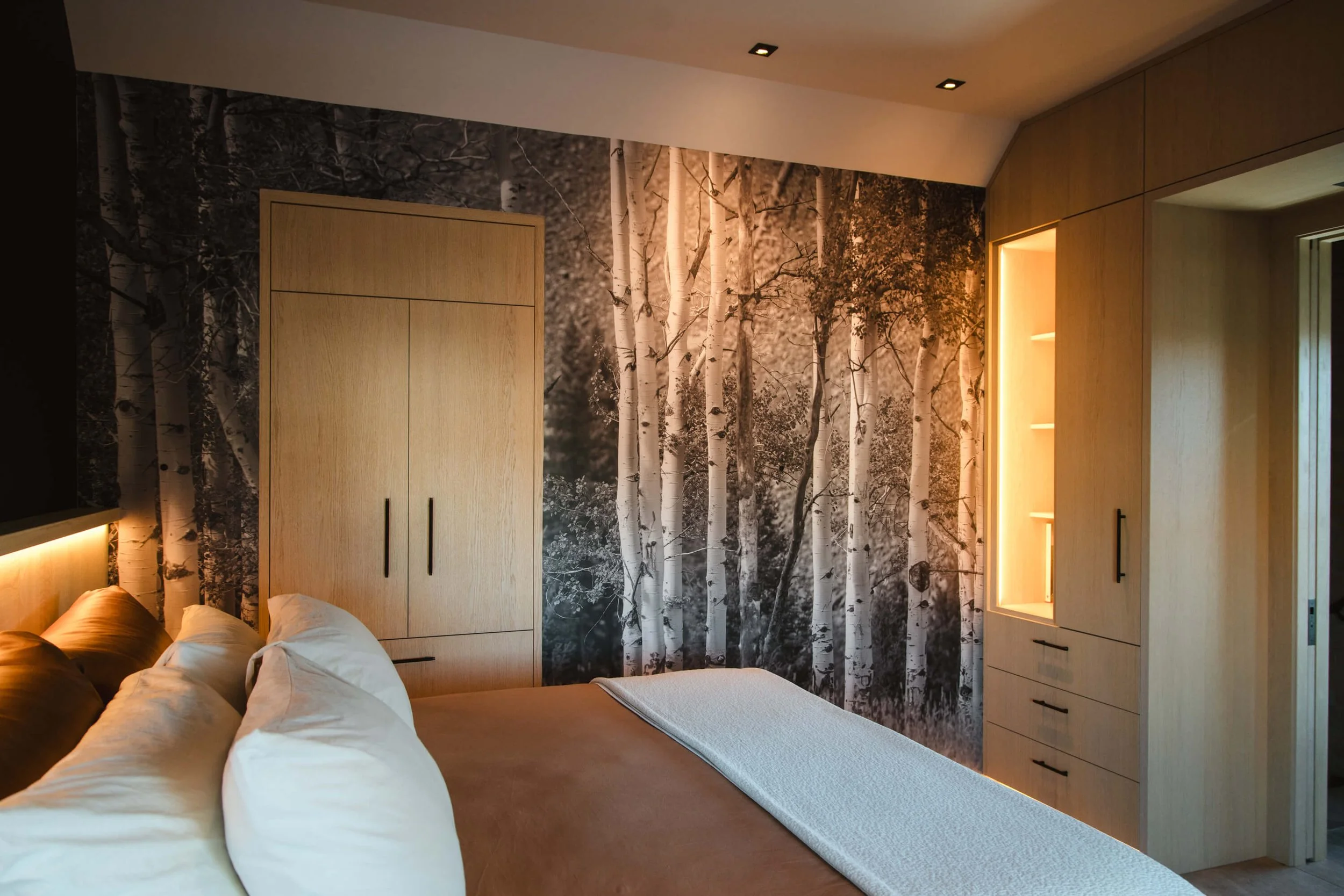 Custom wall wrap with a high-resolution black and white photo of an aspen forest used as a full accent wall behind a bed in a modern, wood-paneled bedroom. Installed by The Wrap Agency at The Rouse House.