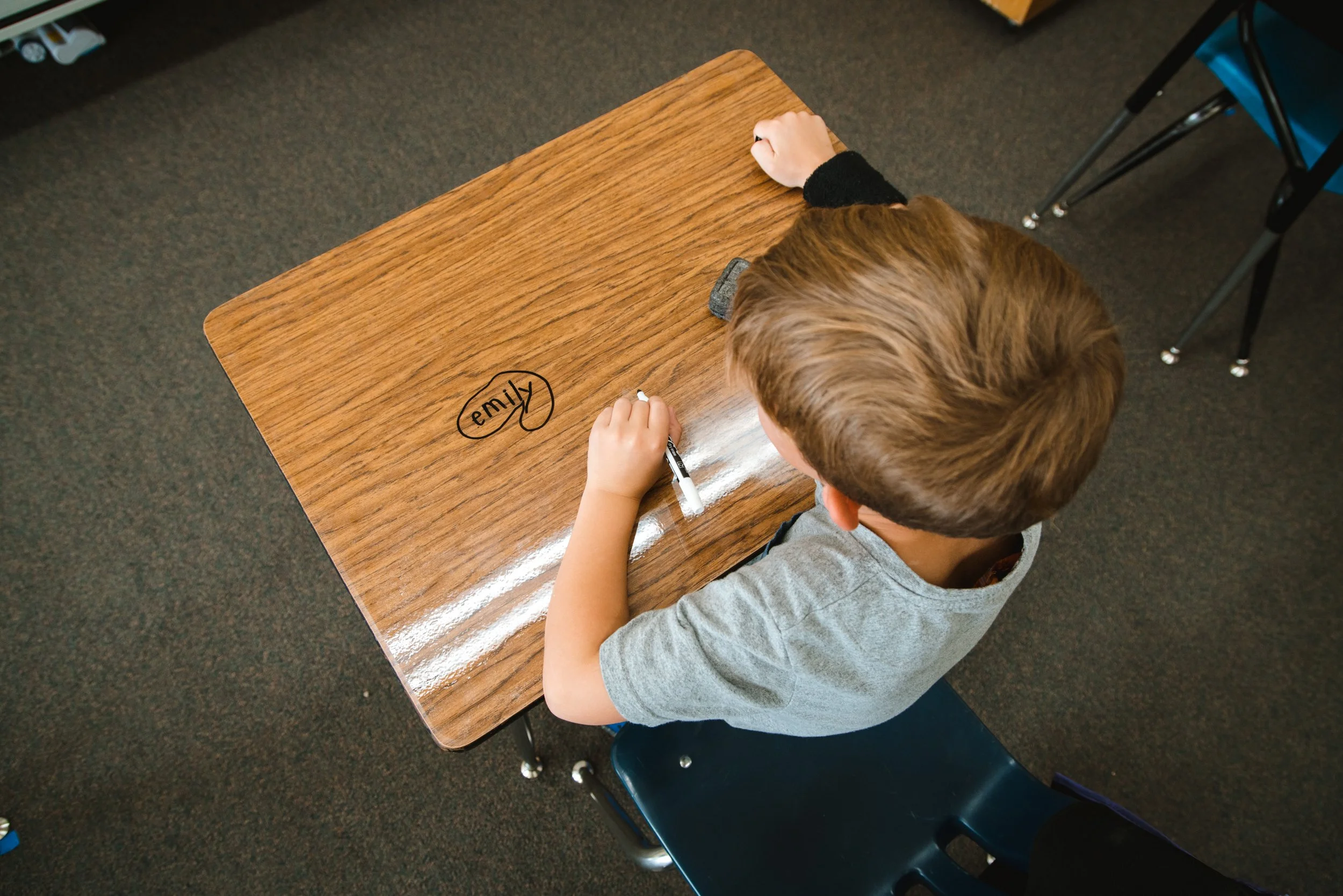 Overhead view of a student adding a circled drawing to a dry erase desktop.