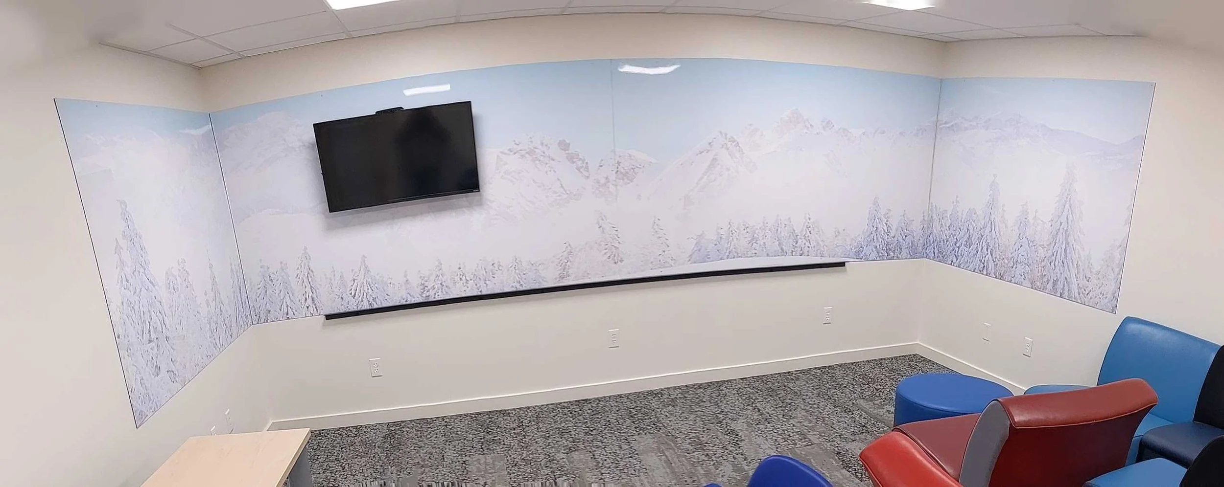 Panoramic view of snowy mountain dry erase wall wraps above a marker rail and colorful chairs.