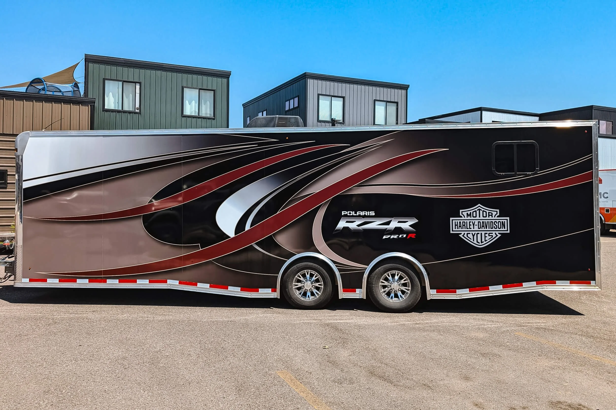 Side view of a trailer wrap with burgundy swooshes on top of of a tan, black and white background. Includes a Polaris RZR logo and Harley Davidson logo