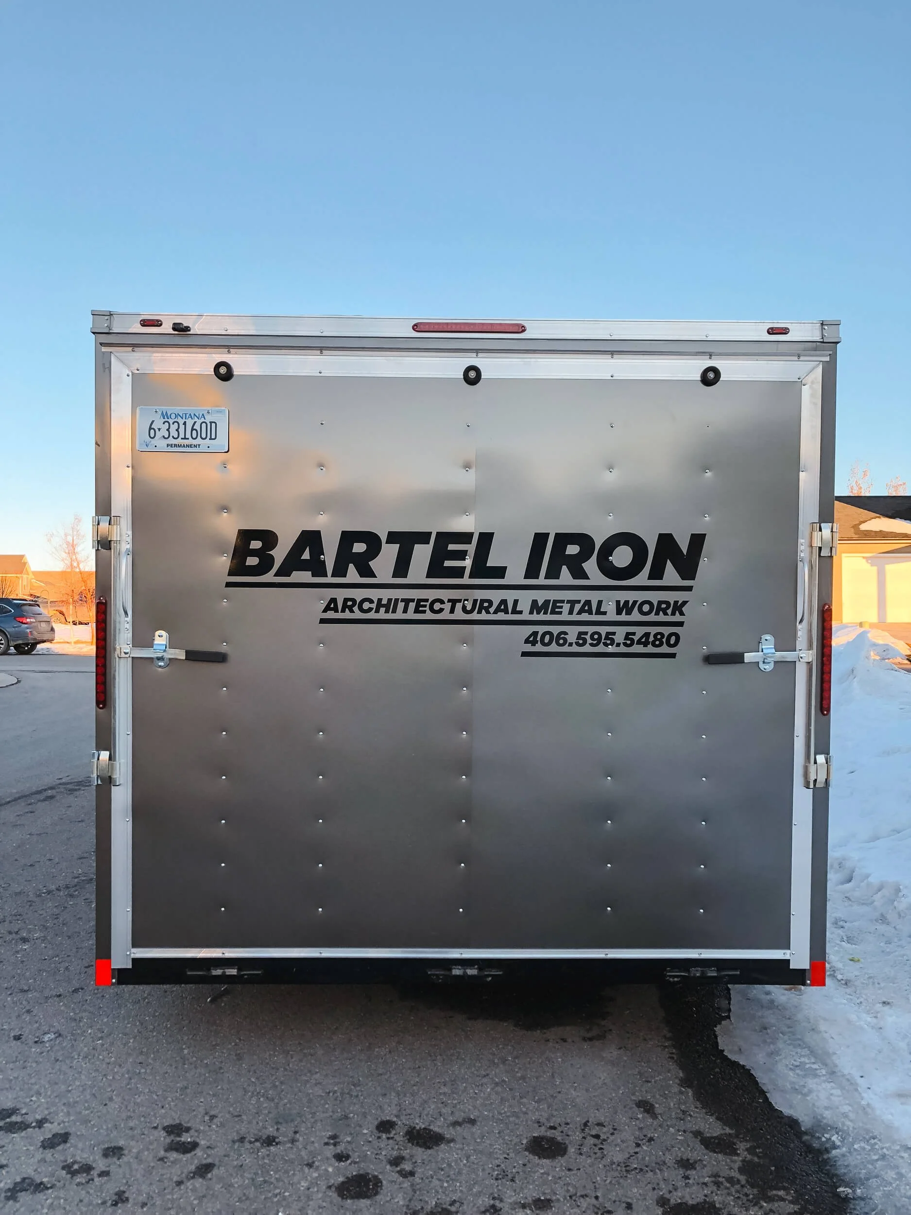 Rear view of a silver trailer with Bartel Iron trailer graphics in Bozeman, Montana, displaying bold black text for architectural metal work and a prominently placed phone number.