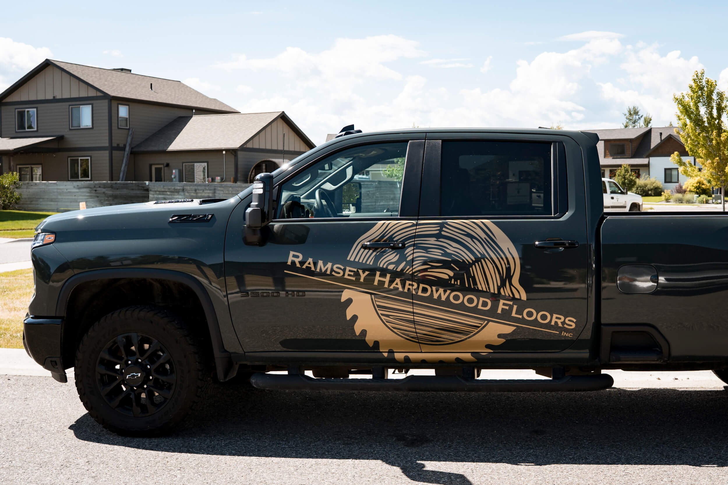 High contrast metallic gold Ramsey Hardwood Floors logo vinyl spot graphics across both doors of dark green Chevy Silverado