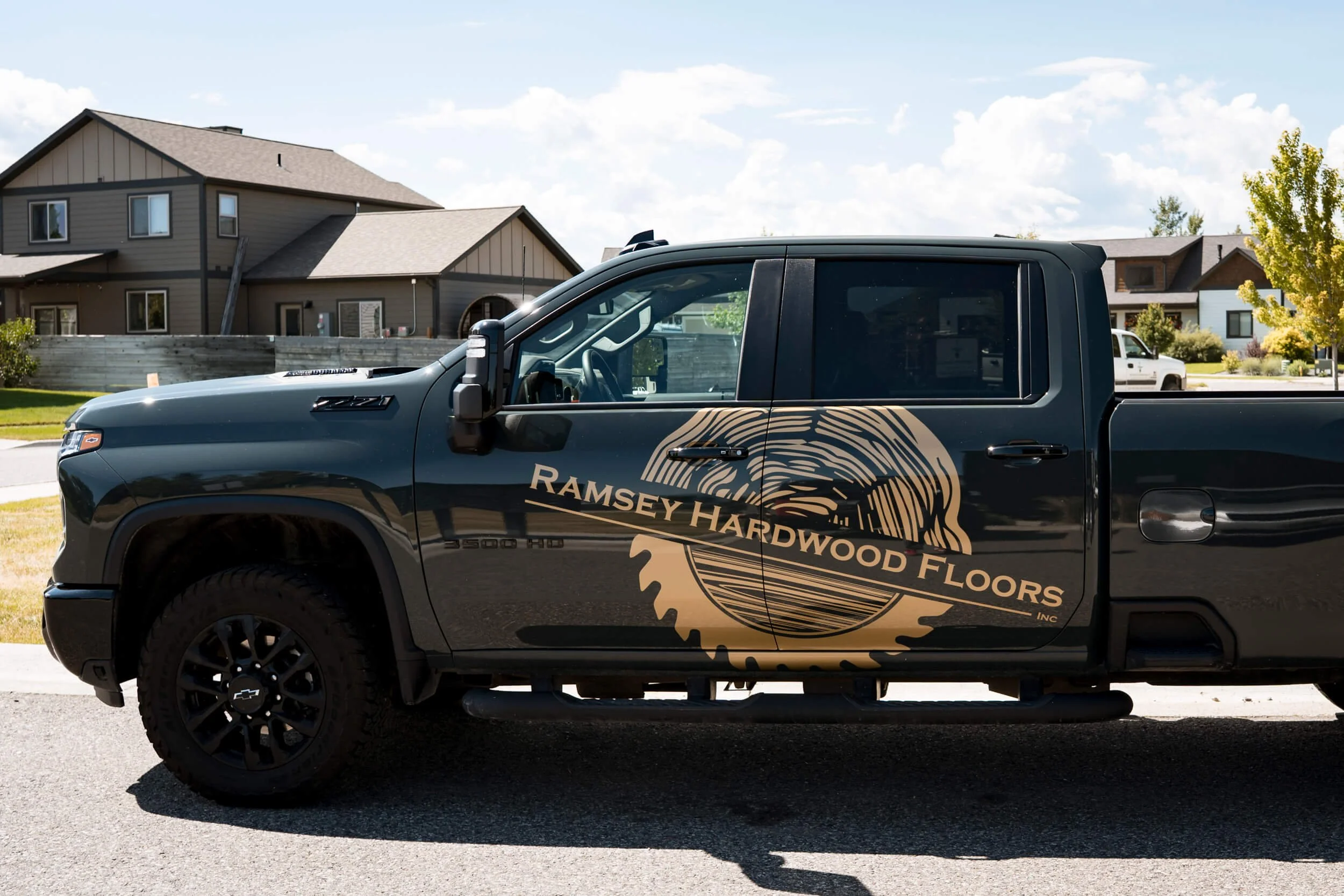 High contrast metallic gold Ramsey Hardwood Floors logo vinyl spot graphics across both doors of dark green Chevy Silverado