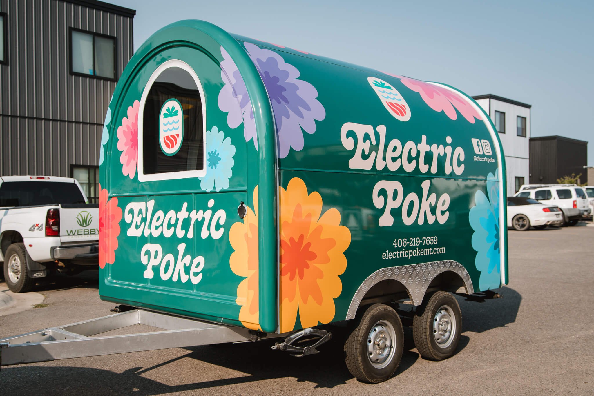 Eye-catching trailer graphics for Electric Poke food trailer in Bozeman, Montana, featuring bold floral designs and white lettering on a vibrant green wrap.