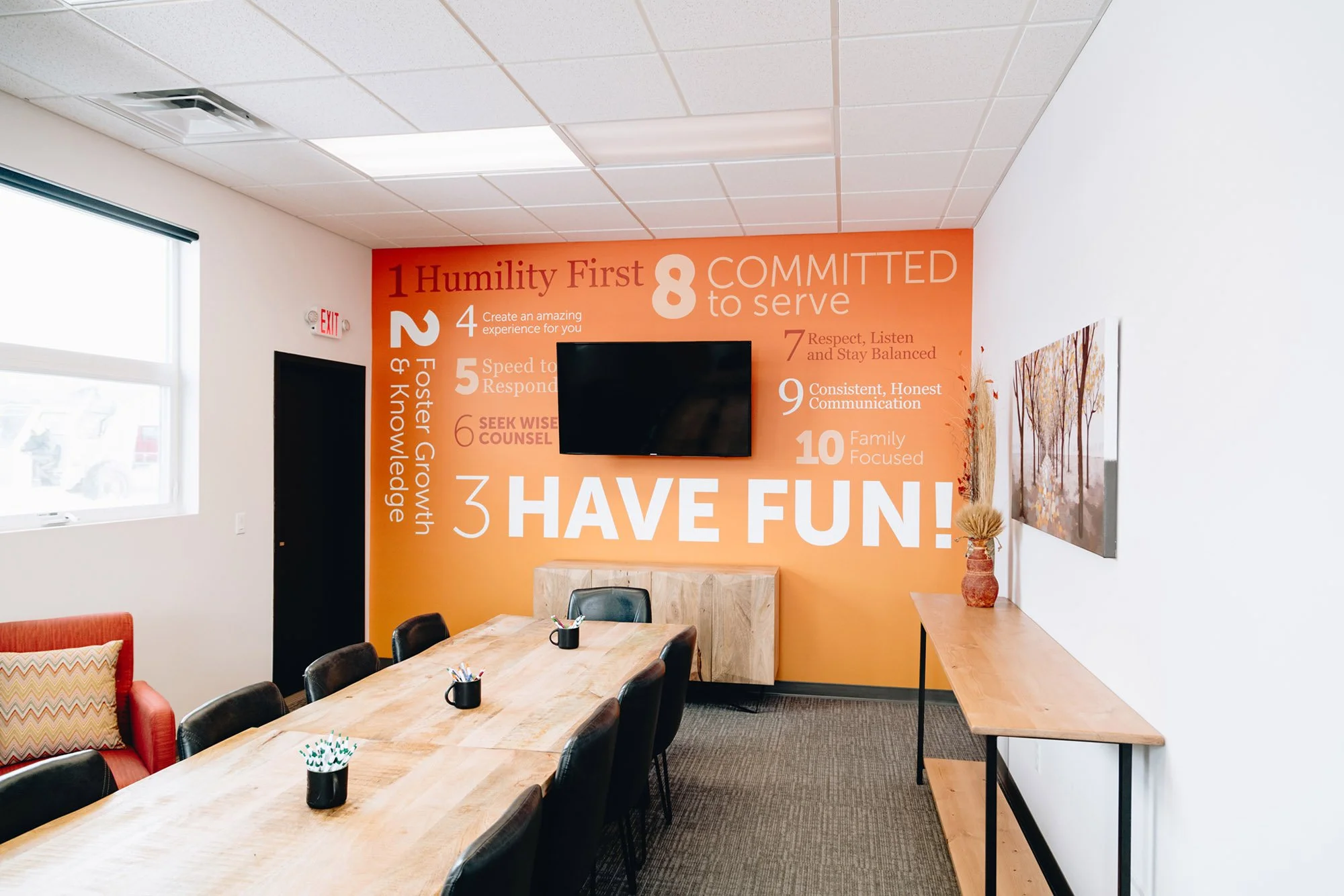 Bold, motivational wall wrap in an office meeting room, featuring an orange background and large-format white typography listing core values like “Humility First” and “Have Fun!” Installed at formerly Fairway Mortgage in Bozeman, MT.