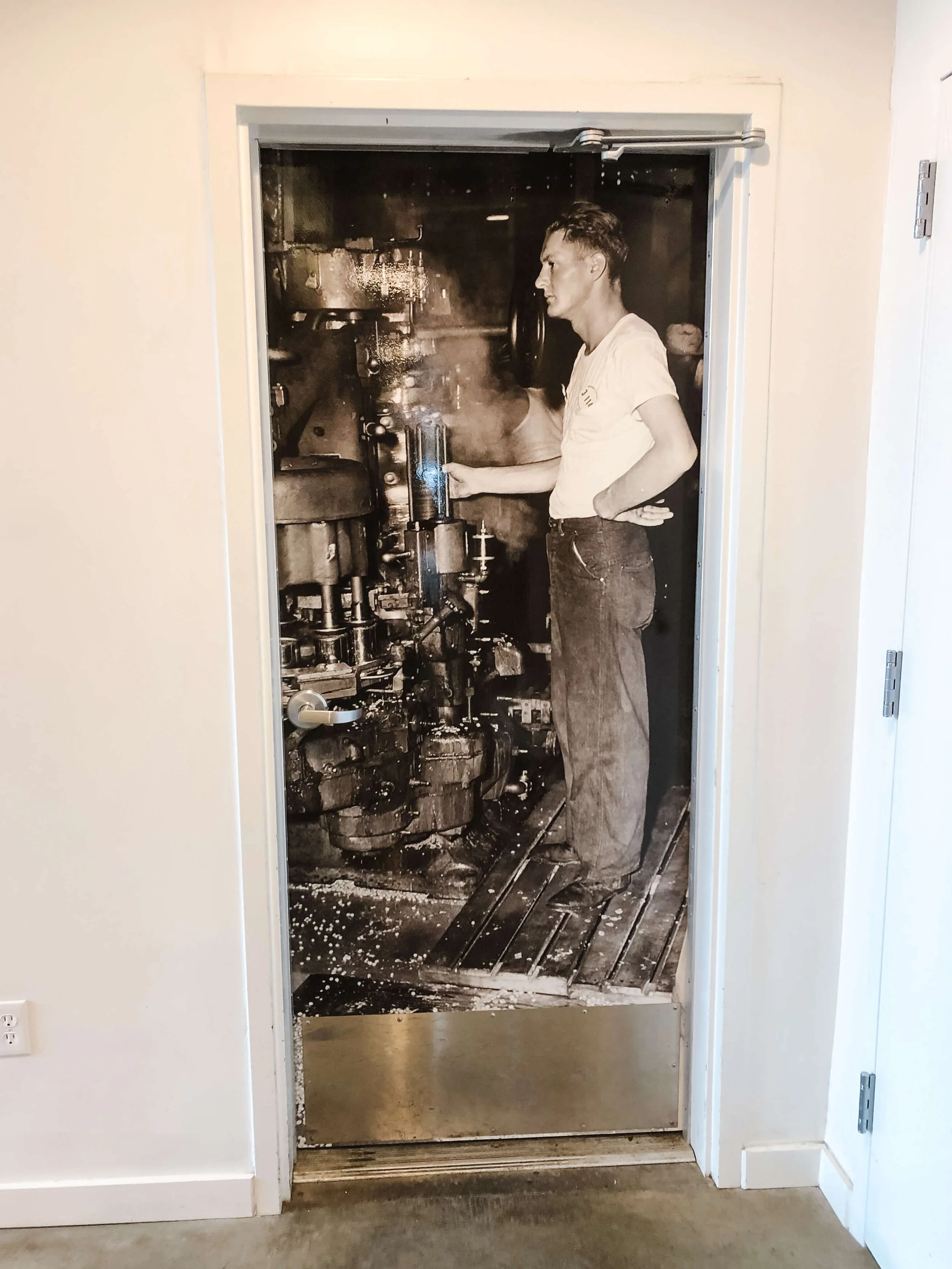 Black-and-white custom vinyl wrap featuring a historic photo of a man operating industrial equipment, applied to a door to add heritage character to the space.