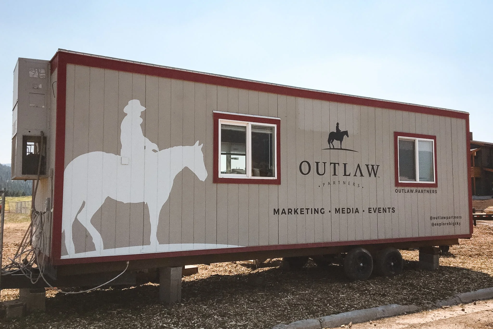 Full trailer wrap for Outlaw Partners in Bozeman, Montana, with tan and red paneling, white silhouette of a cowboy on horseback, and bold marketing text. 