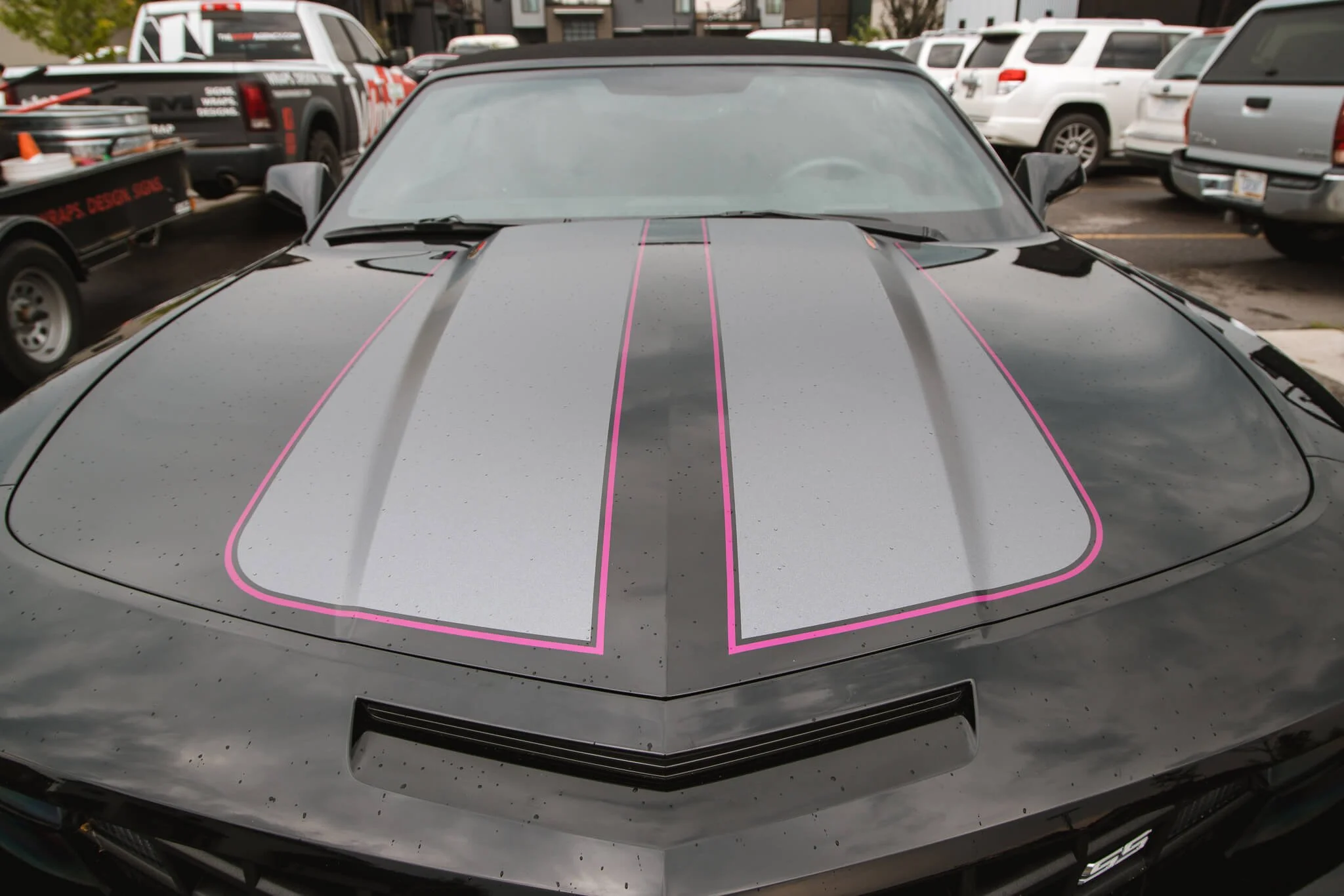 Custom hood wrap on a black Camaro featuring dual silver racing stripes with hot pink outlines for high-contrast visual appeal. Installed in Bozeman, Montana.