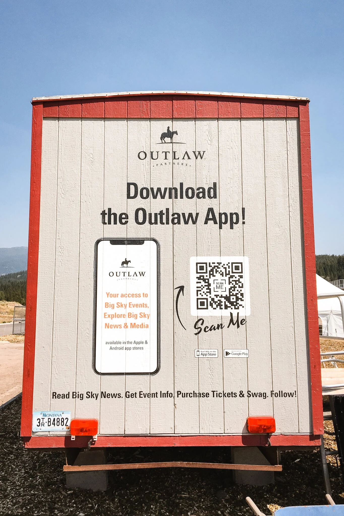 Rear trailer graphics for Outlaw Partners in Bozeman, Montana, promoting their mobile app, including QR code, large logo, and event details in bold type.