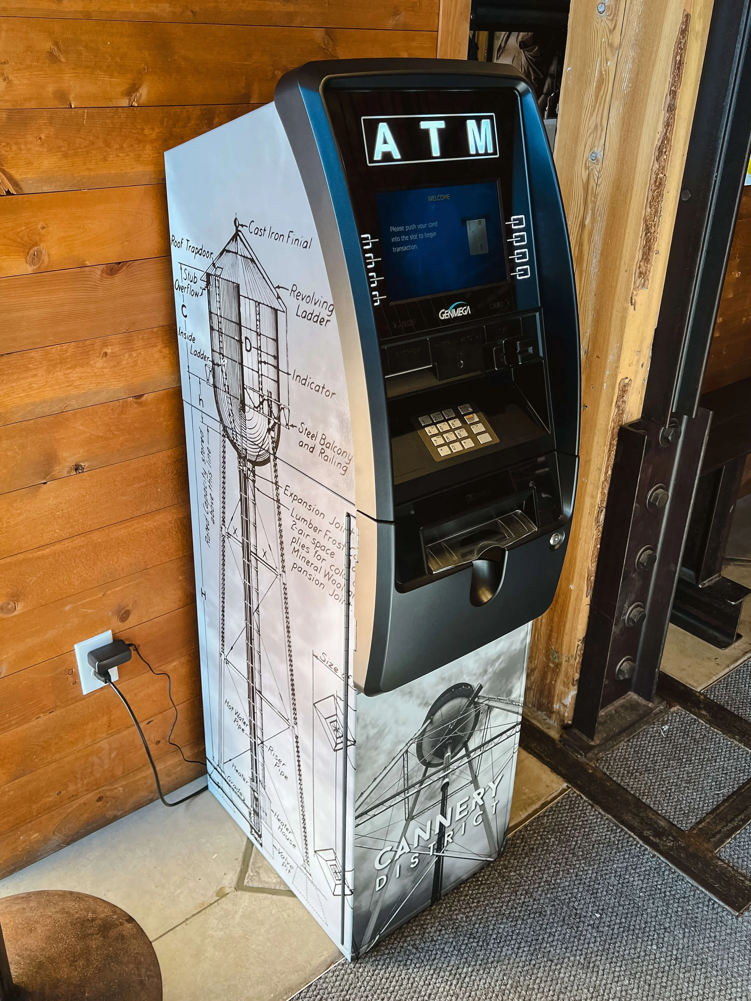 Custom vinyl wrap on an ATM featuring technical illustrations and a water tower sketch with Cannery District branding, turning utility into marketing.