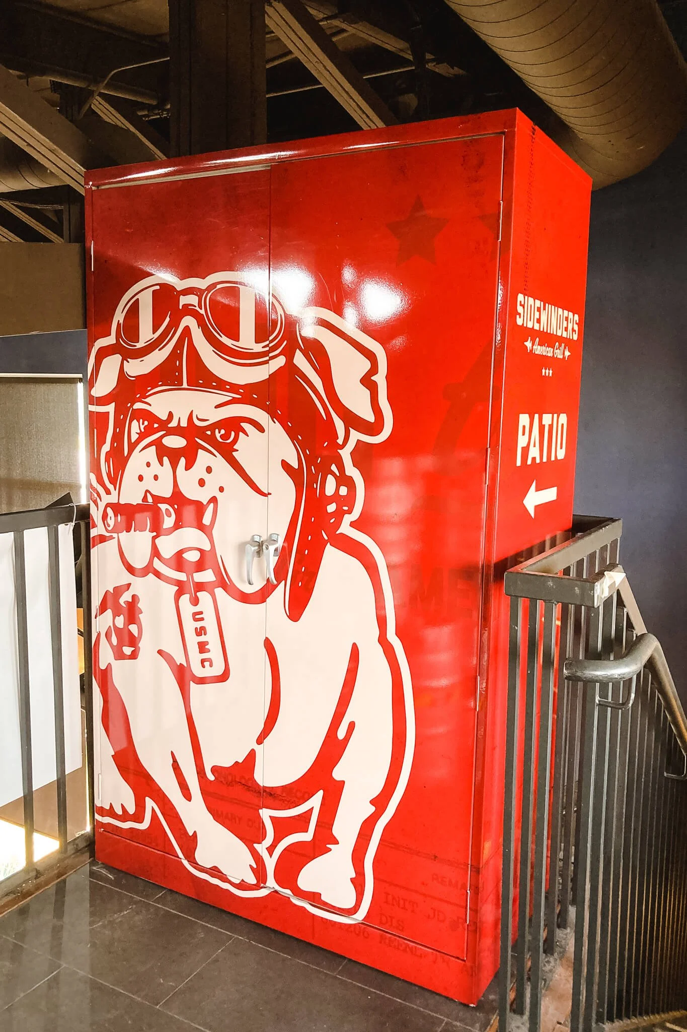 Eye-catching red wall wrap featuring a graphic bulldog mascot and directional arrow to patio. Custom vinyl wraps for restaurants and branded spaces.