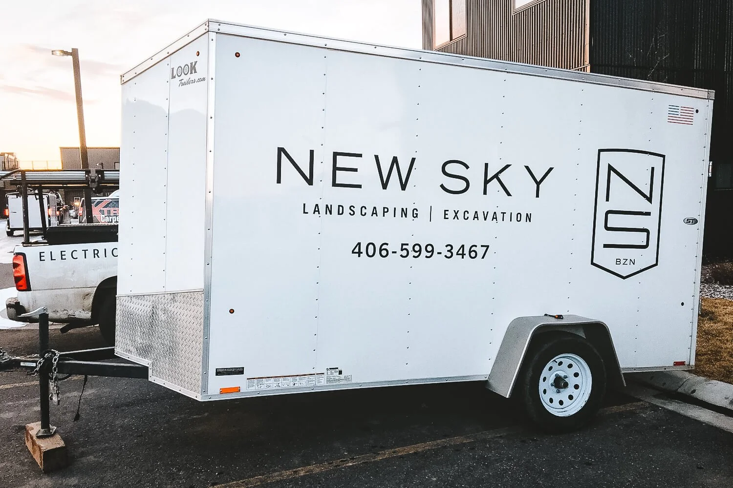 New Sky Landscaping trailer graphics in Bozeman, Montana, on a white wrap with minimalist black logo, shield emblem, and business phone number displayed prominently. 