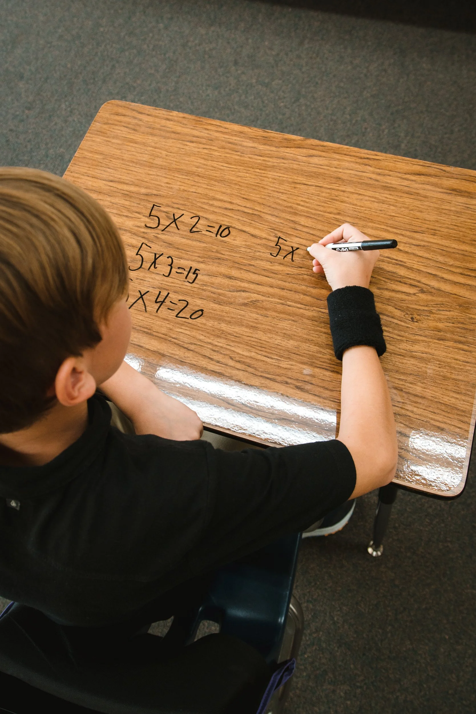 Math equations written in black marker across a woodgrain dry erase desktop.