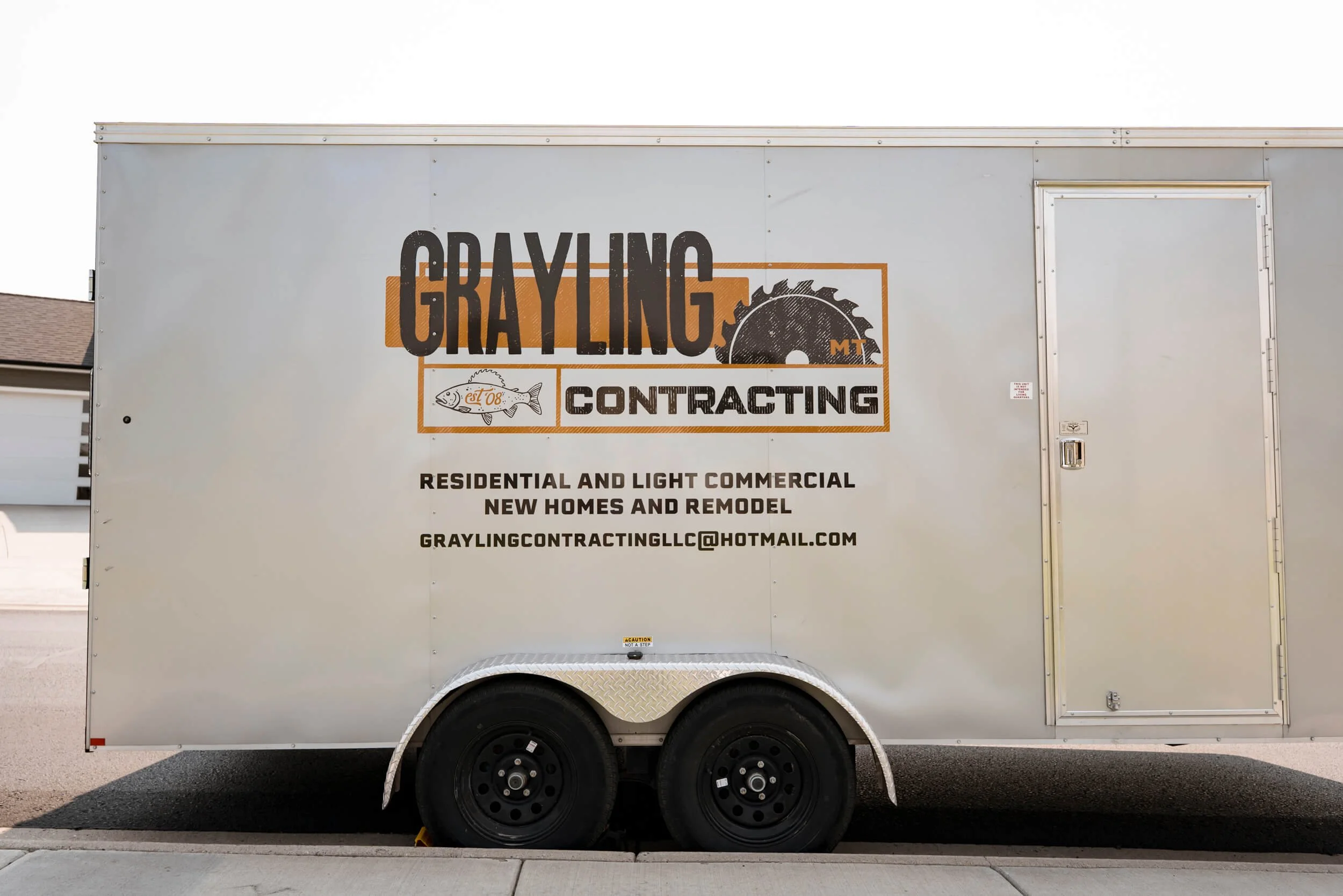 Black and gold Grayling Contracting logo with services and contact info beneath on the side of a silver trailer