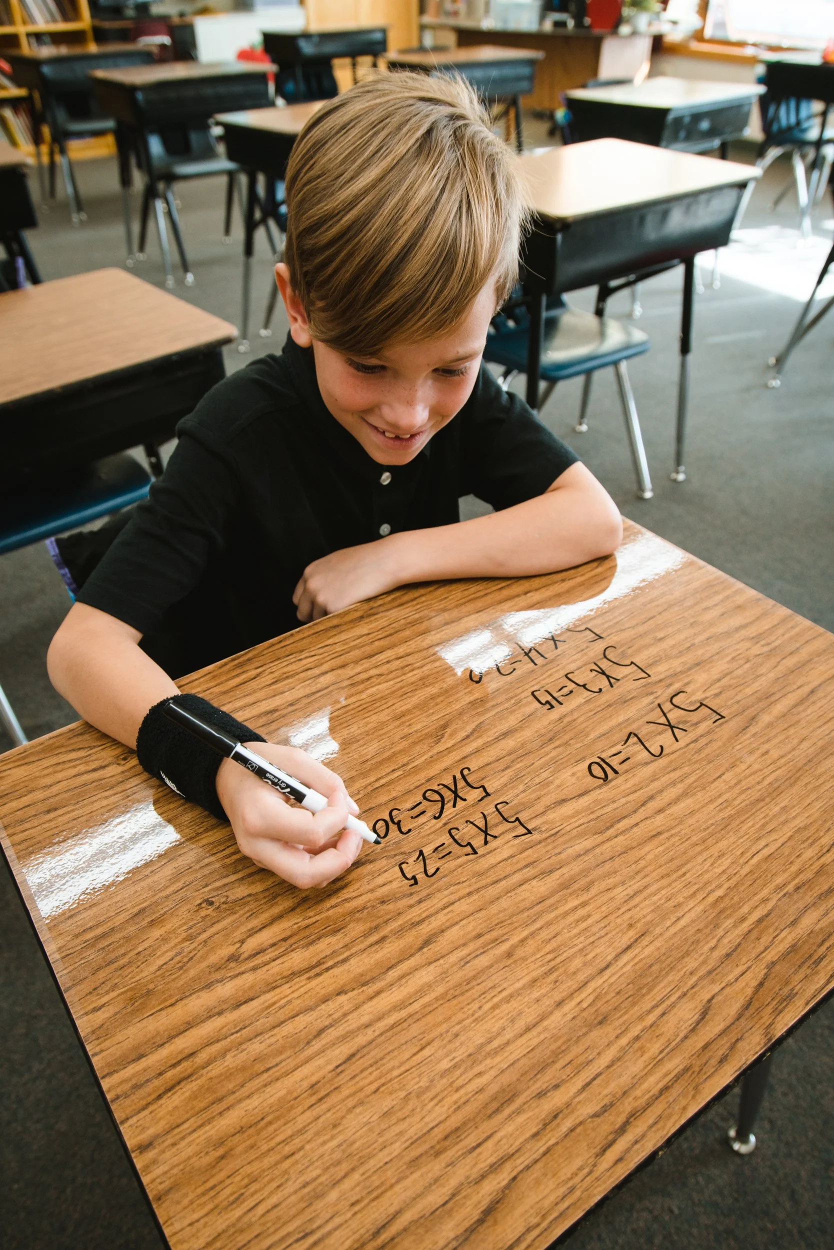 Student smiling while writing math problems on a wrapped dry erase desk.