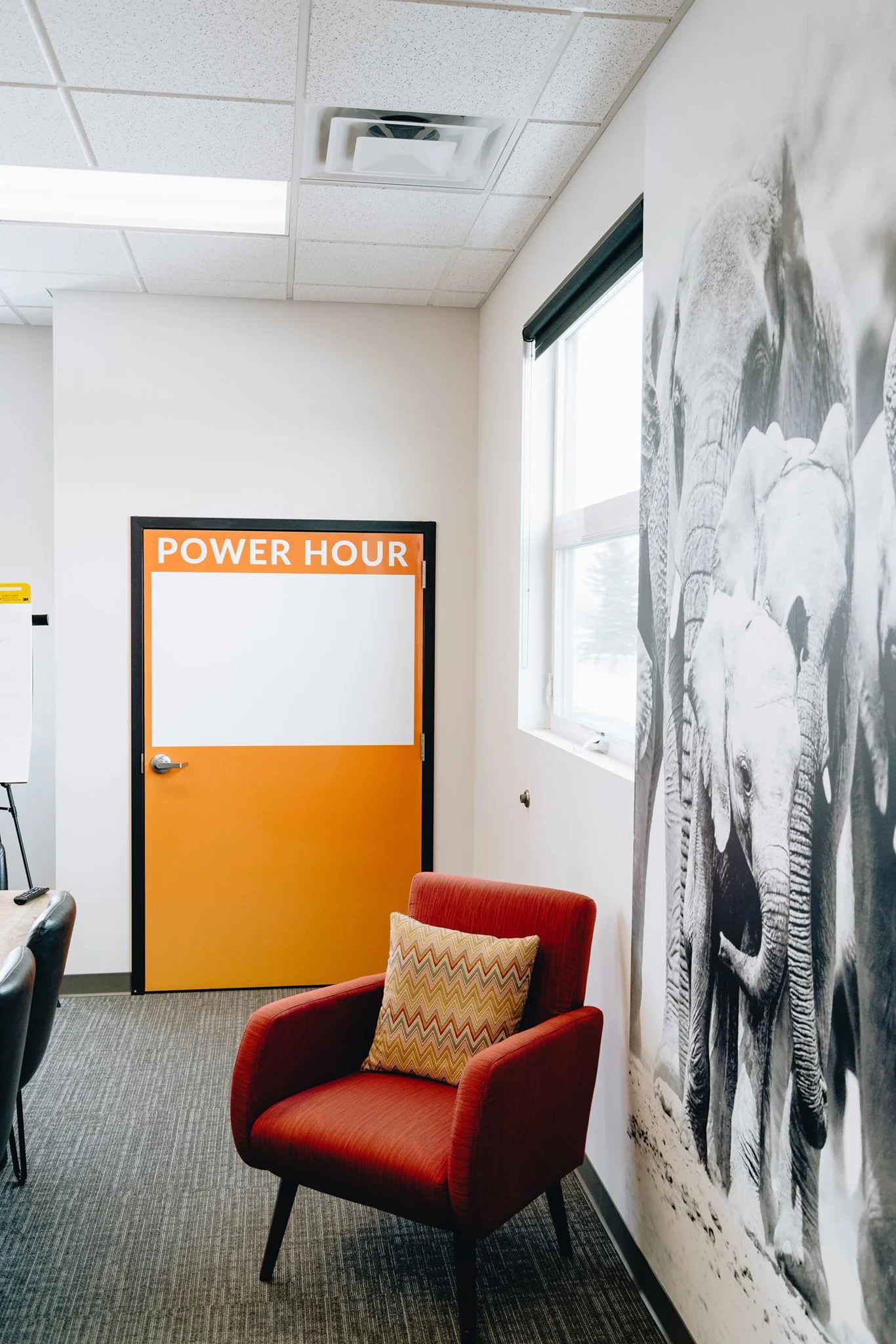 Orange office door with a white dry erase panel and “POWER HOUR” lettering beside a red chair.