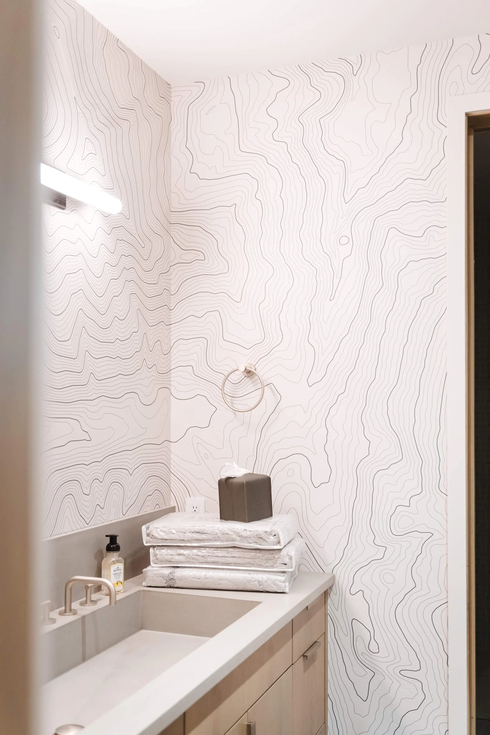 Modern bathroom with Lone Peak topographic map wall vinyl, light wooden cabinetry, and a sleek white sink.