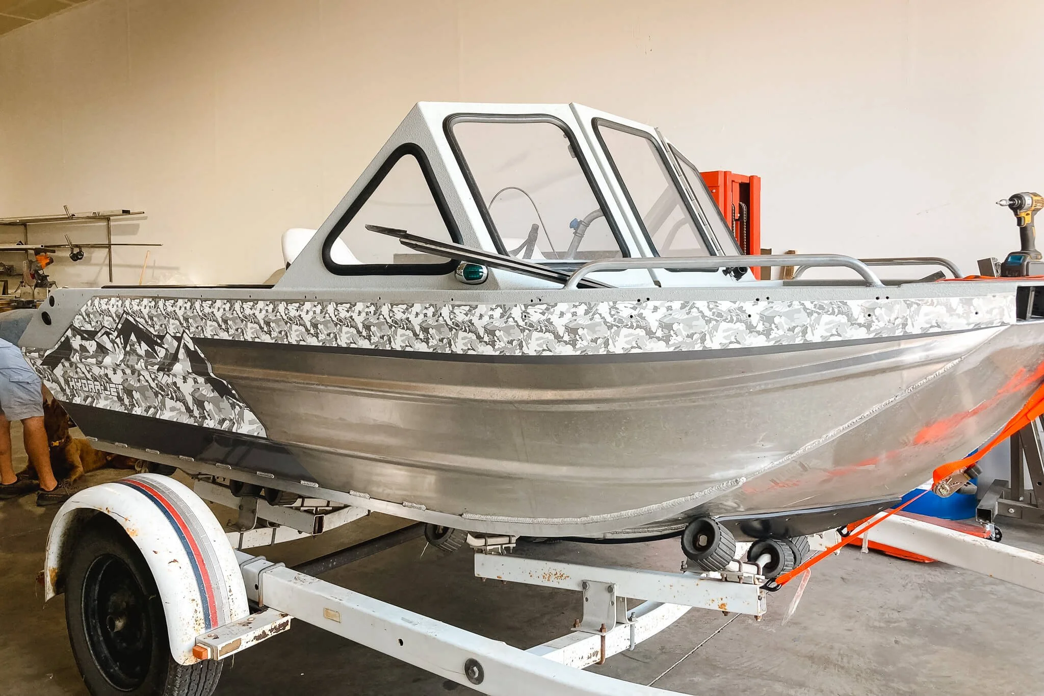 Angled front-side view of a silver jet boat with camouflage-style custom vinyl wrap across the sides, located in Bozeman, MT.