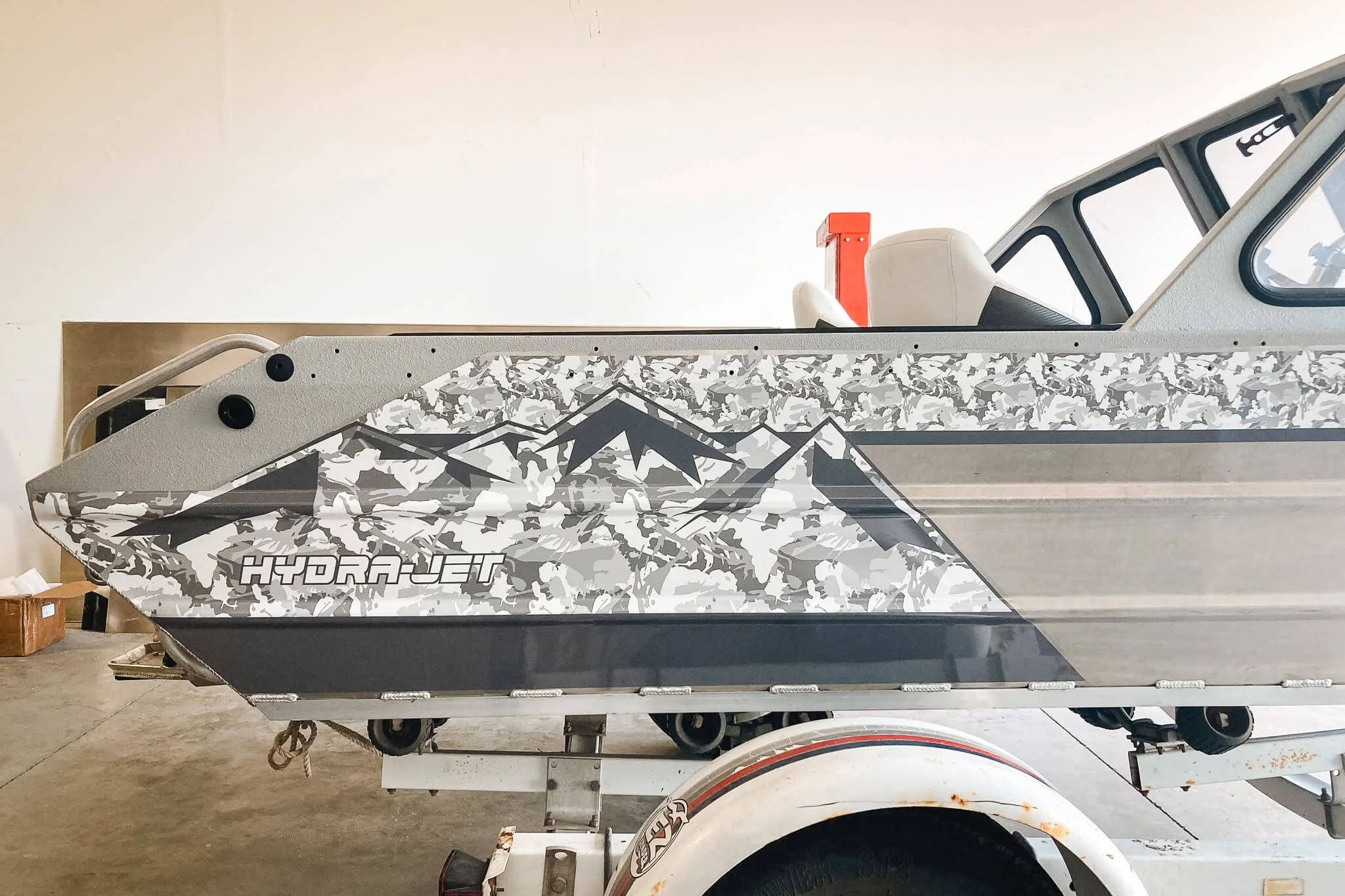 Side view of a metallic silver jet boat featuring a mountain landscape pattern in grayscale custom vinyl wrap design in Bozeman, MT.
