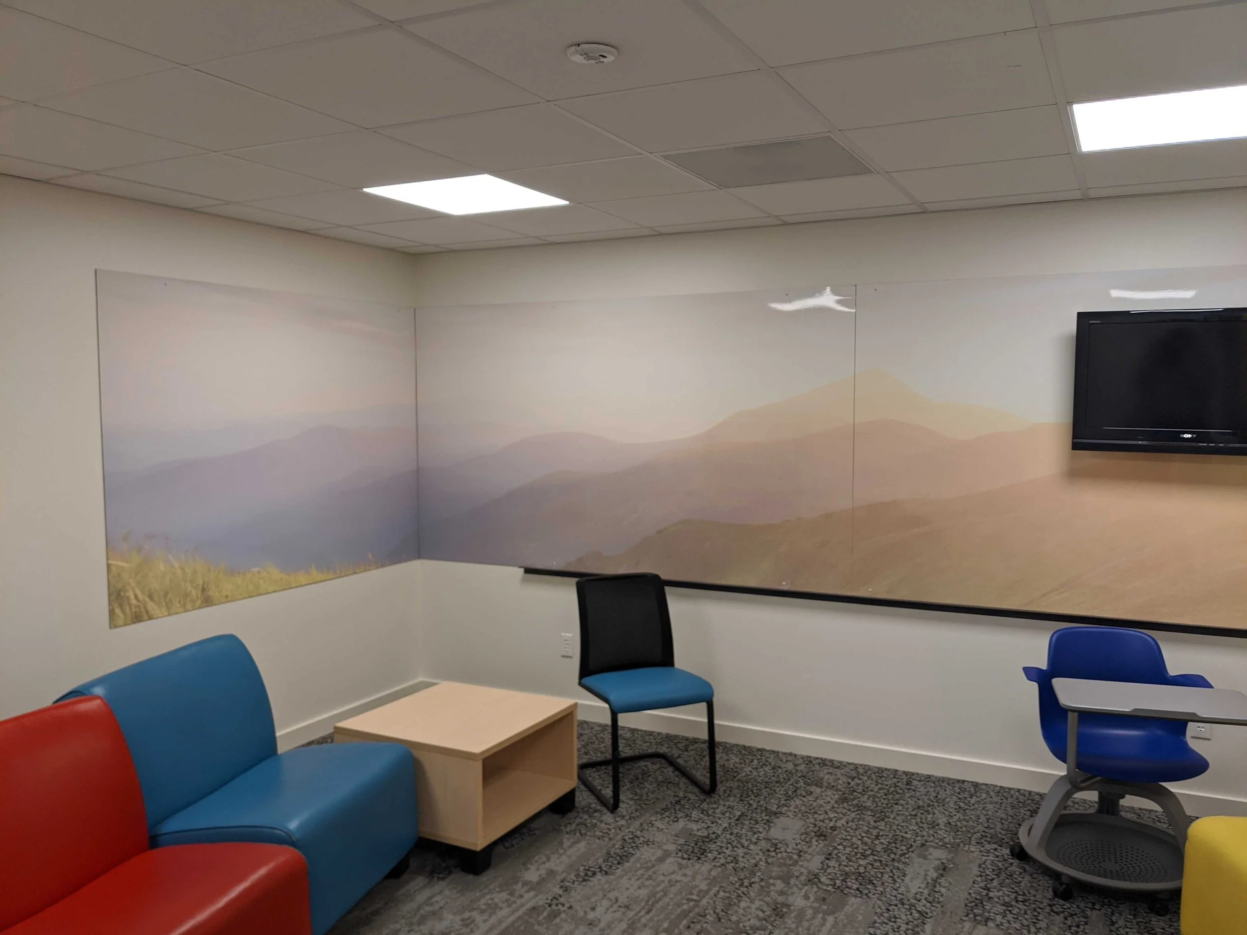 Custom dry erase wall coverings with layered mountain scenery above red and blue seating.