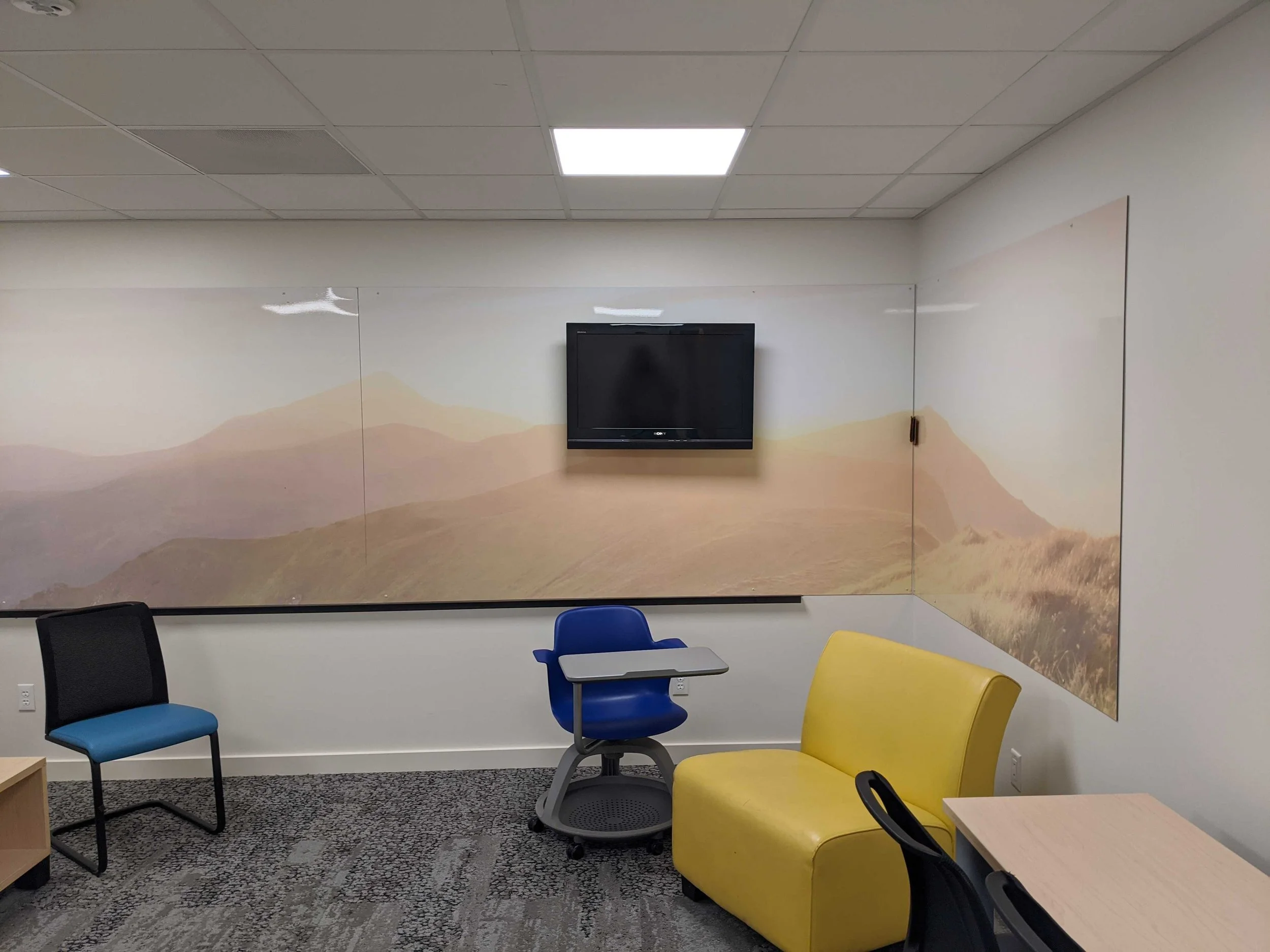 Mountain landscape dry erase wall graphic behind a mounted screen, with yellow seating in the foreground.