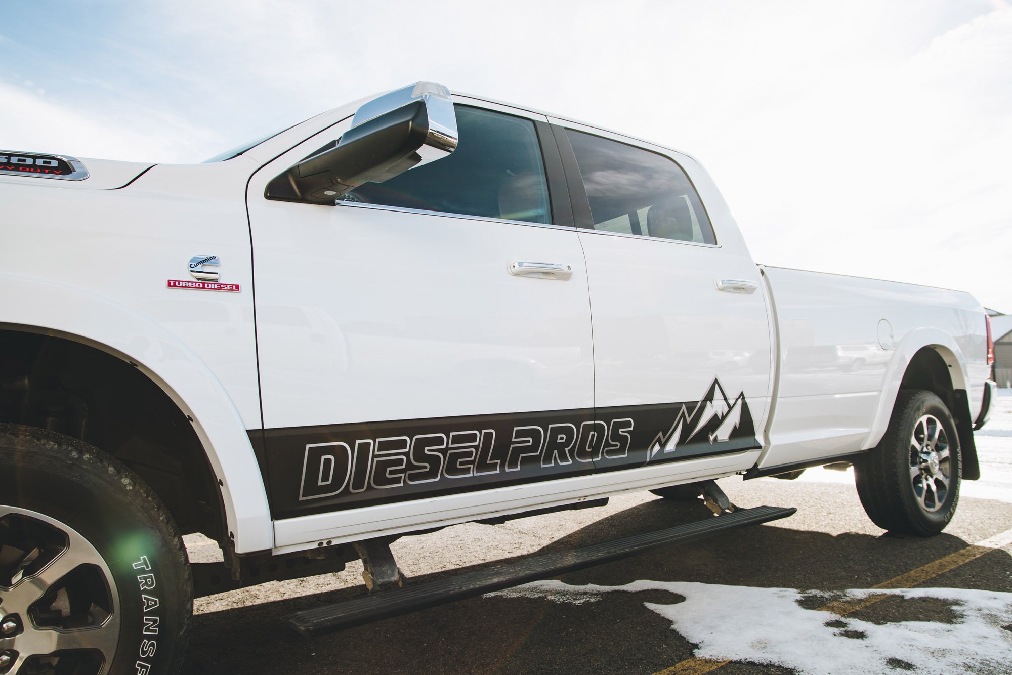 White Dodge Ram truck with black and white DIESEL PROS logo and custom mountain-themed graphic, demonstrating a rugged and professional vehicle wrap for a diesel shop in Bozeman, Montana.