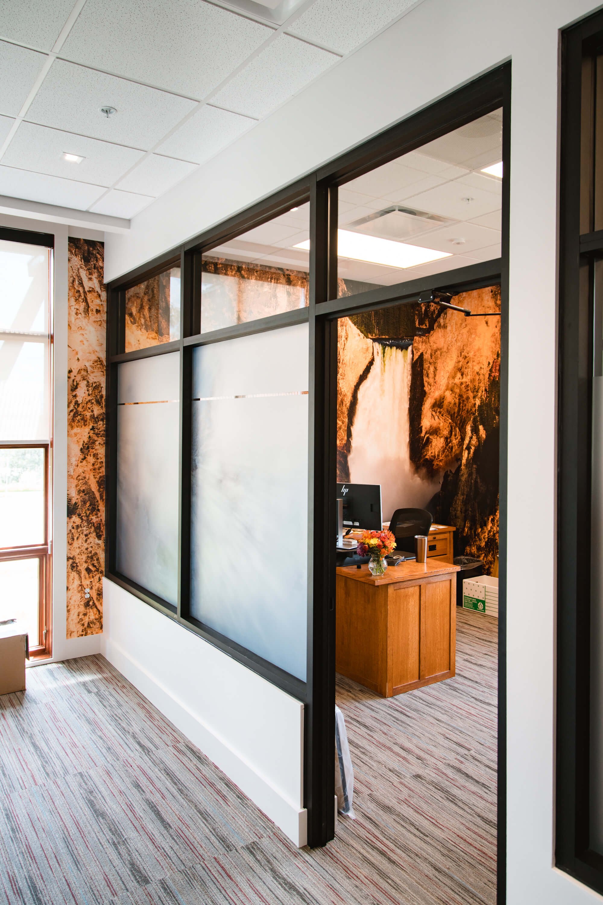 Immersive wall wrap of a waterfall cascading down a rugged cliff face, creating a dynamic and calming atmosphere in a glass-walled executive office. Installed at Yellowstone Forever in Bozeman, MT.