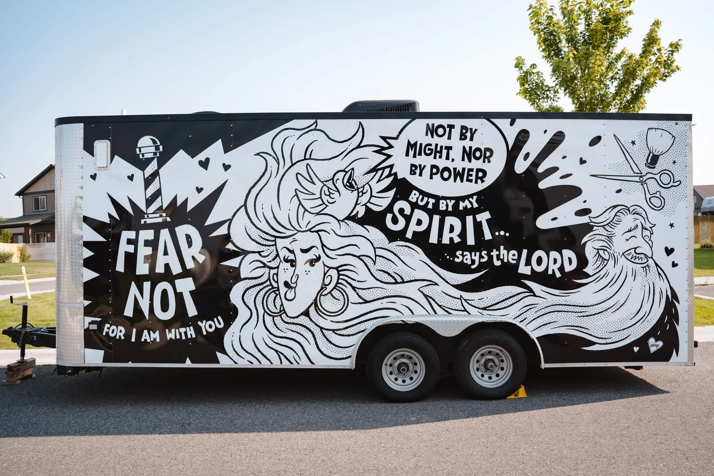 Side view of barbershop trailer in Bozeman, Montana, with custom black-and-white comic mural featuring scissors, lighthouses, scripture quotes, and stylized hair illustrations.