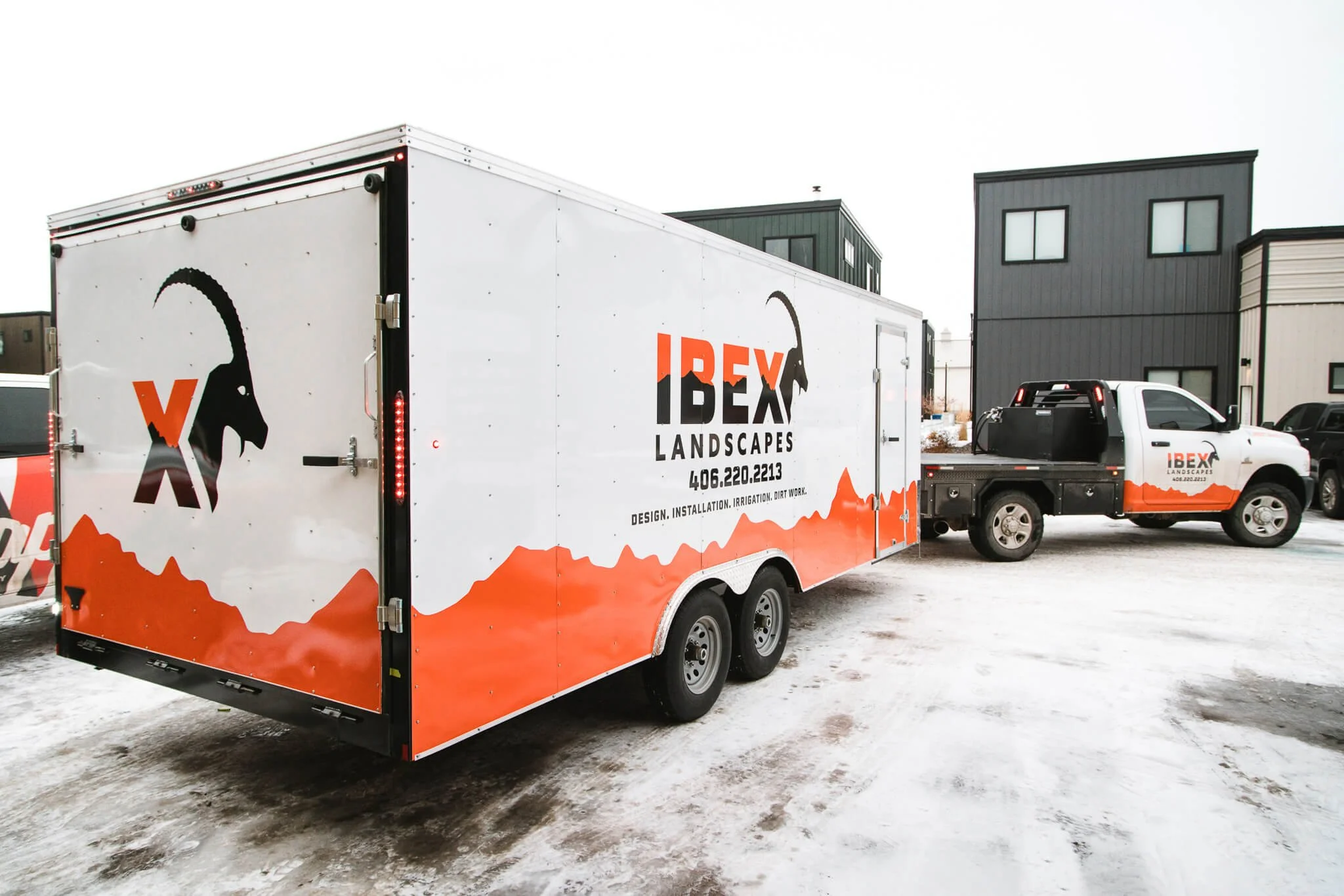 Branded trailer graphics for IBEX Landscapes in Bozeman, Montana, featuring a white background with orange mountain silhouettes, a black ibex logo, and business contact details applied to both trailer and adjacent truck.