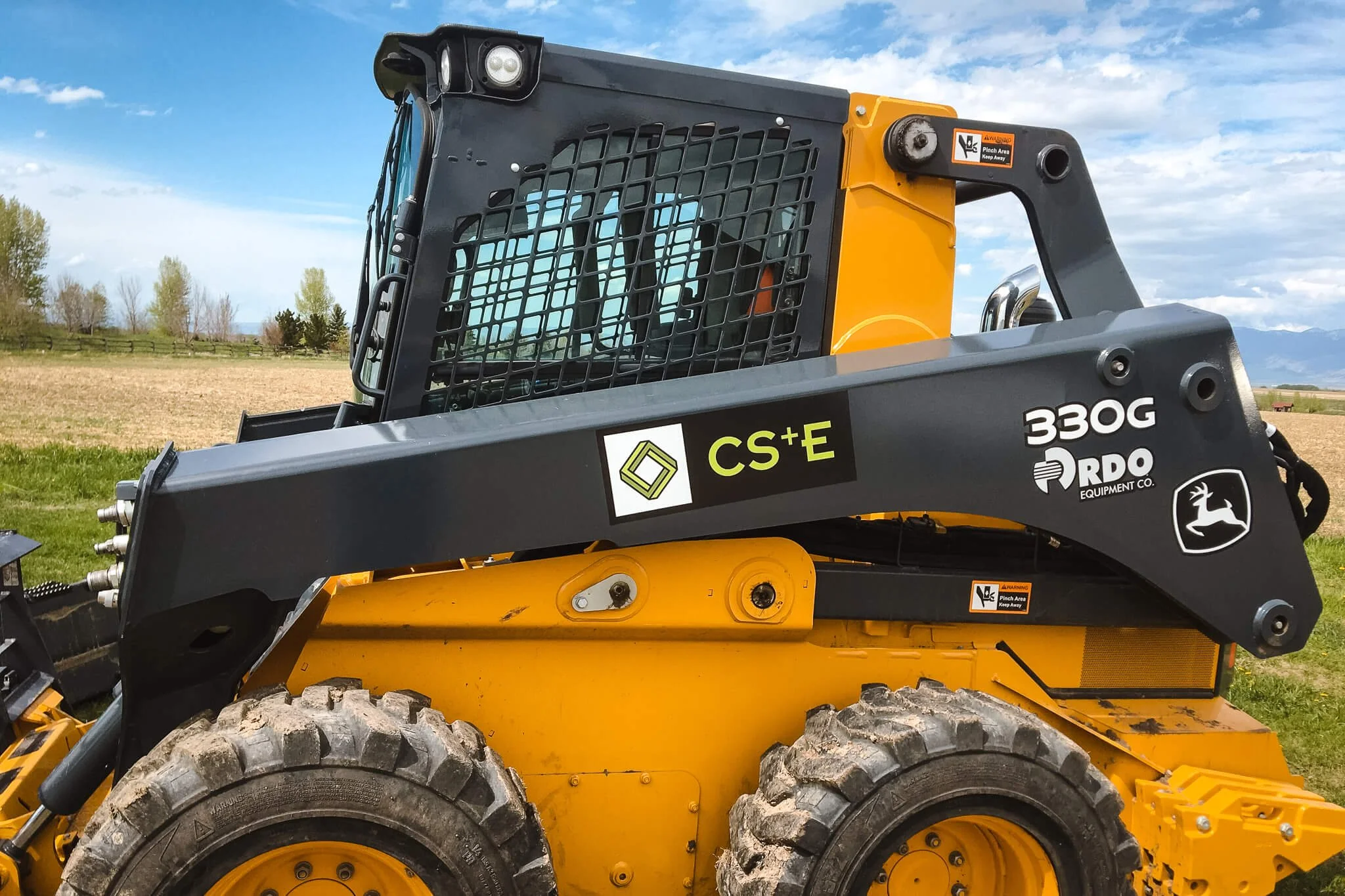 Side view of a John Deere 330G skid steer featuring custom vinyl wraps with CS+E logo and RDO Equipment Co. branding. Custom vinyl wraps for construction equipment.