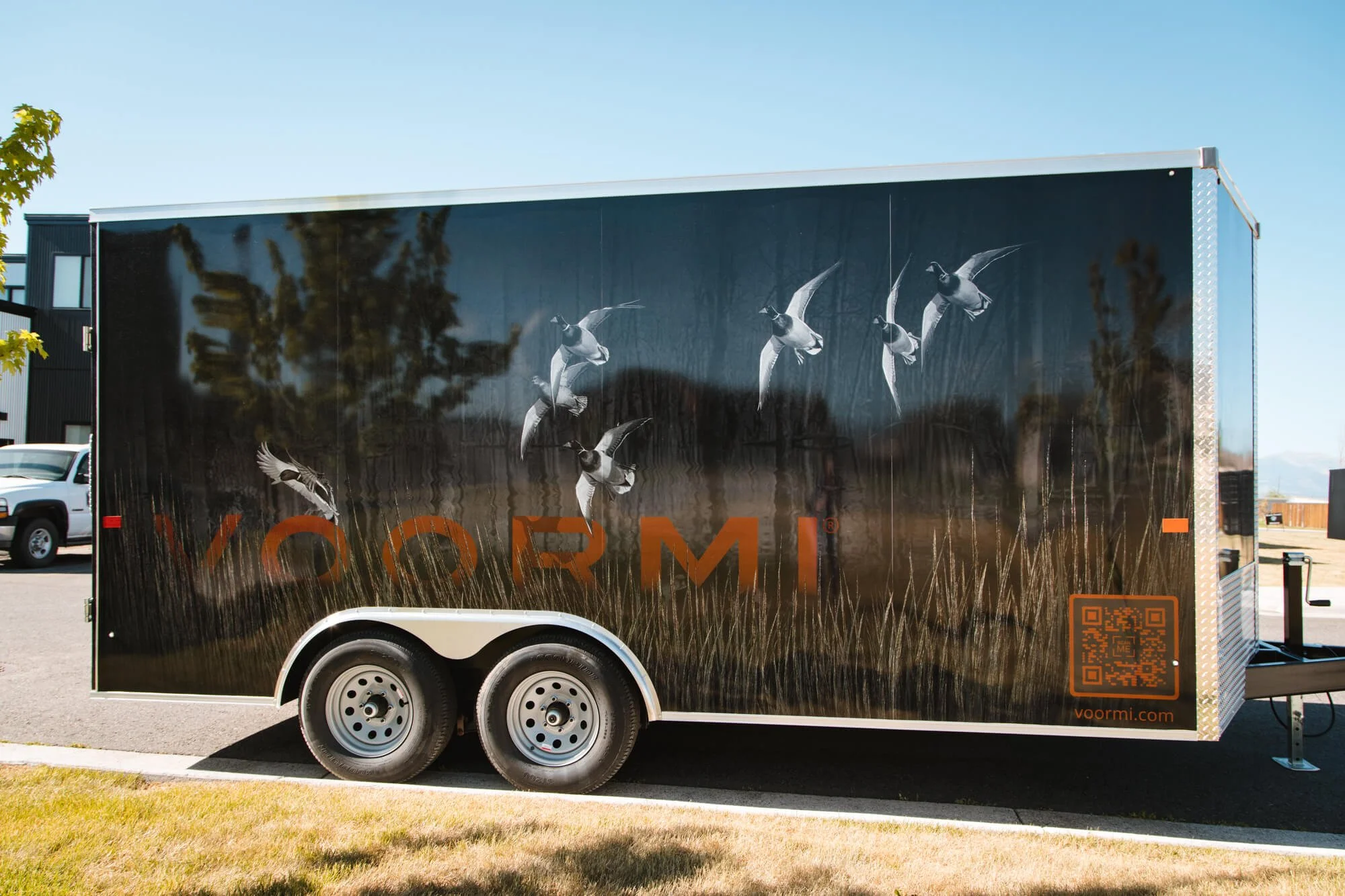 Side trailer wrap for VOORMI in Bozeman, Montana, with a vivid print of ducks in flight over tall prairie grass, seamlessly incorporating the logo and QR code in the trailer graphics.