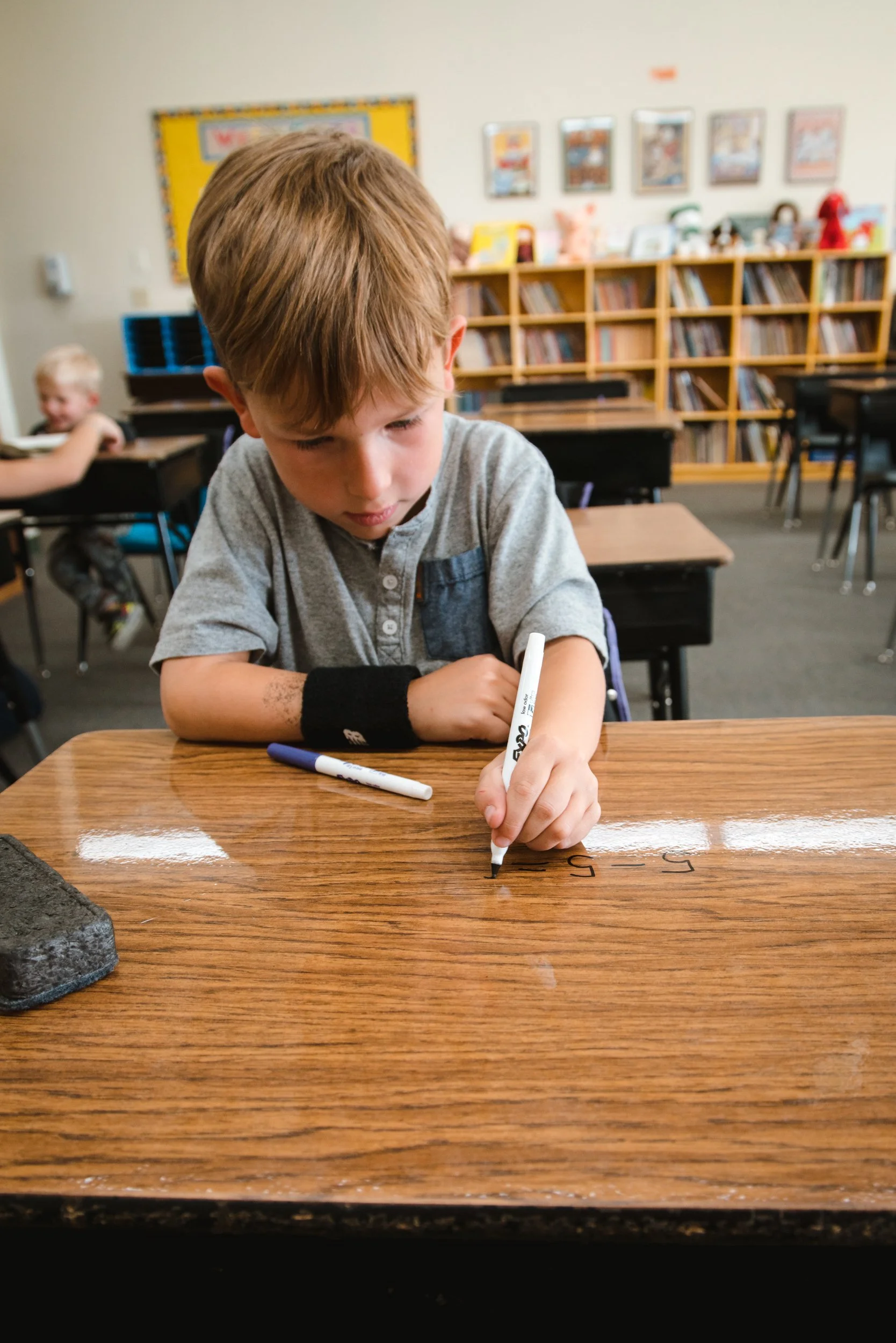 Front view of a student writing math problems directly on a dry erase desktop.