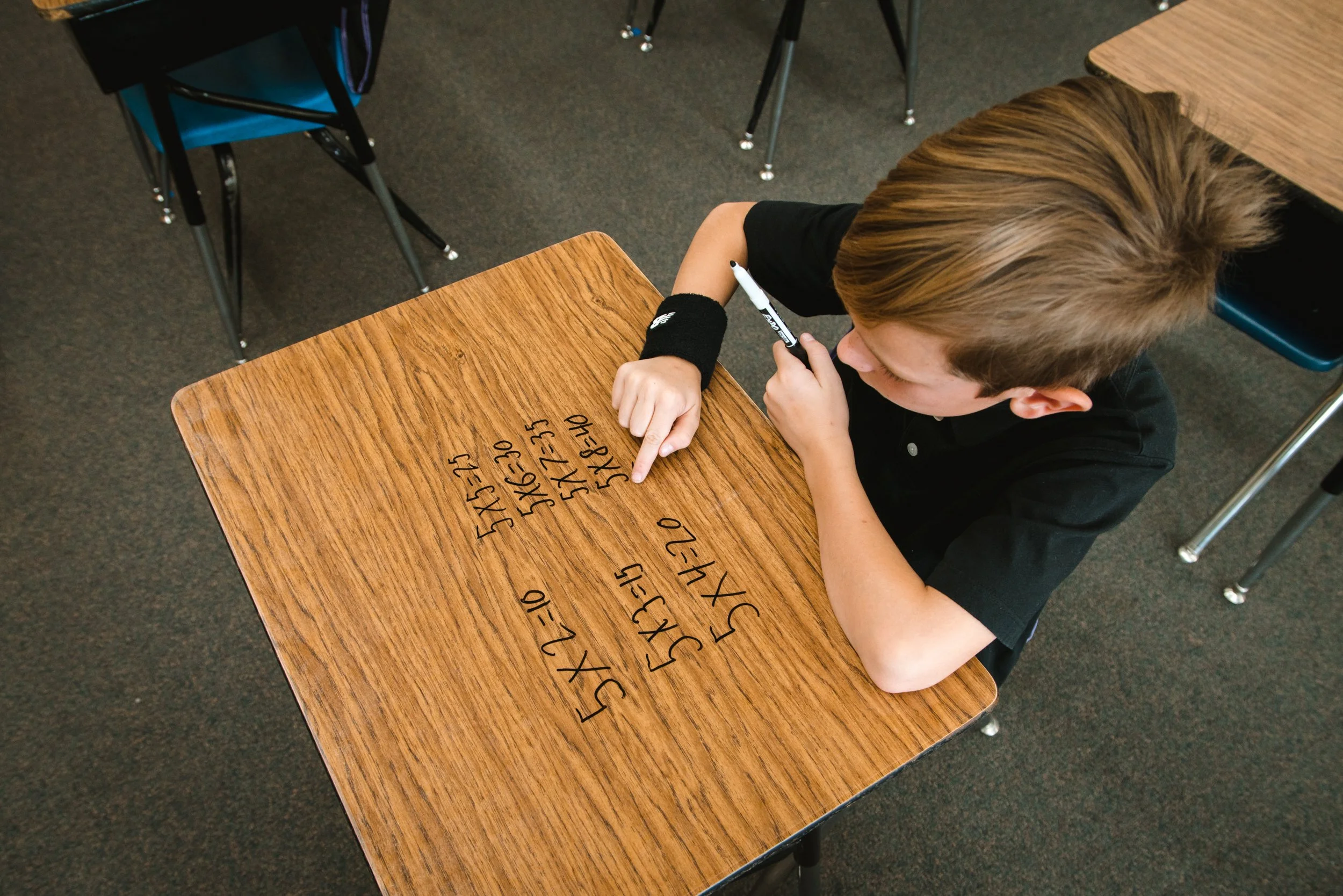 Overhead view of a student erasing math problems from a woodgrain dry erase desktop.