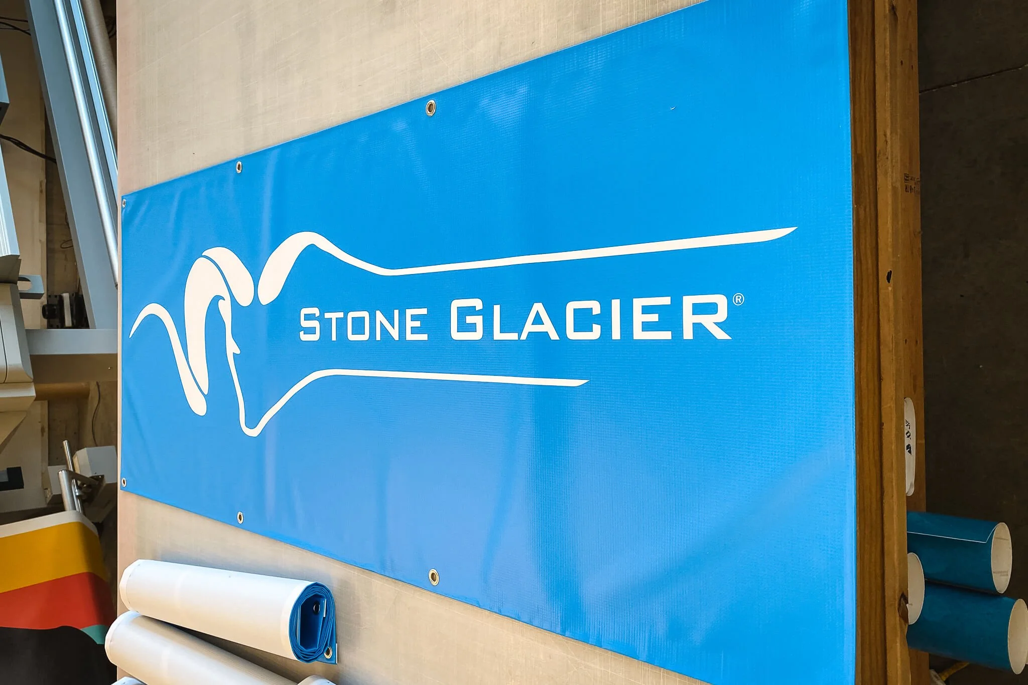 Mounted vinyl banner with the Stone Glacier logo featuring a stylized mountain goat design in white on blue.