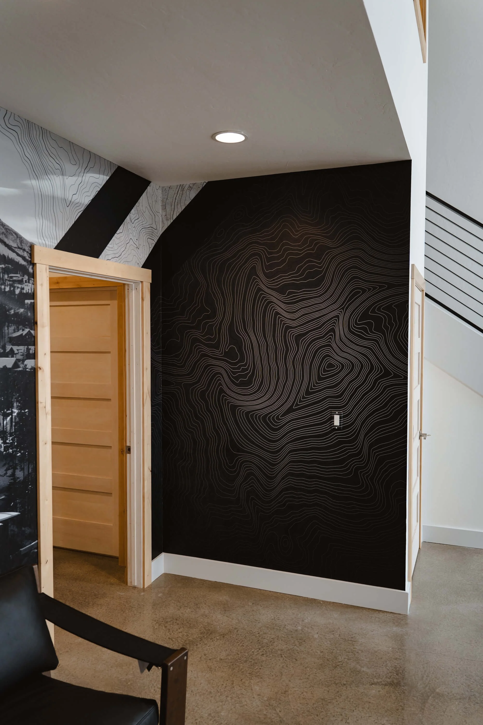 Minimalist topographic black wall wrap with subtle contour line details in a hallway corner, blending branding with modern interior design at Momentum Customs in Bozeman, MT.
