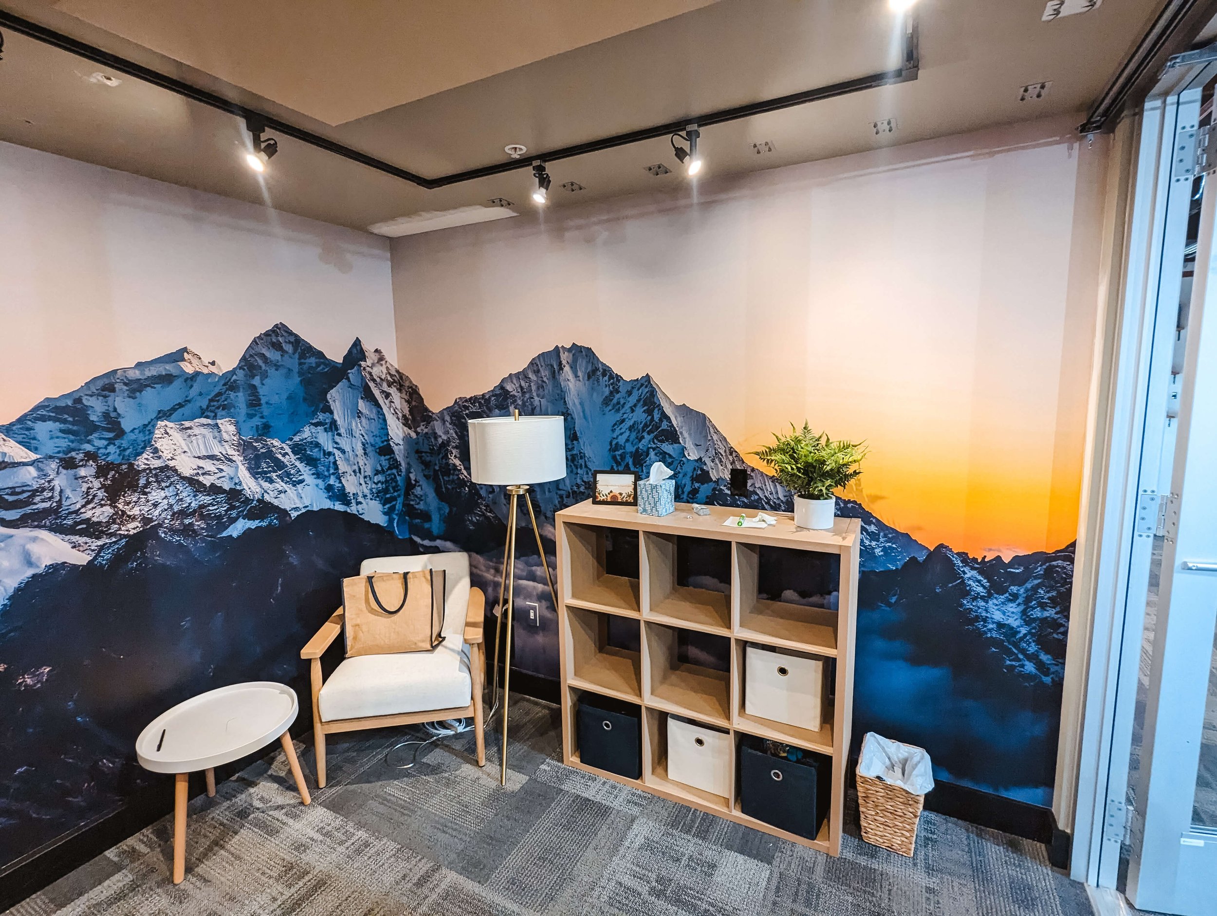 Alternate view of the wellness room showcasing a golden sunset on the mountain wall mural and soft natural lighting across the neutral-toned decor. Location: Bozeman, MT.