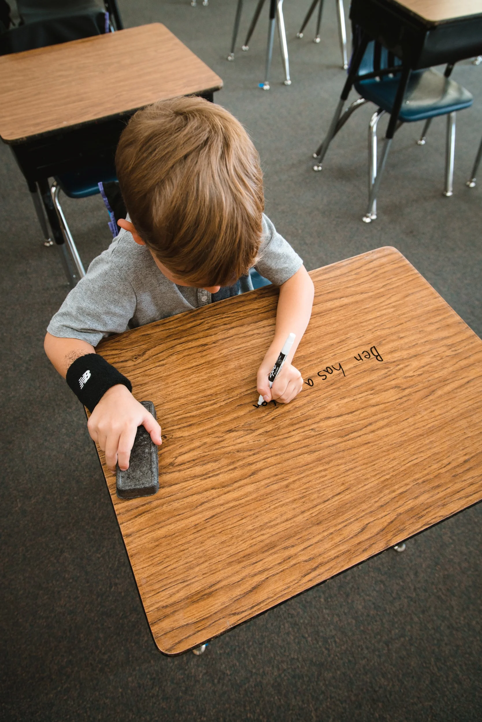 Student writing on a dry erase desk while holding an eraser in the other hand.