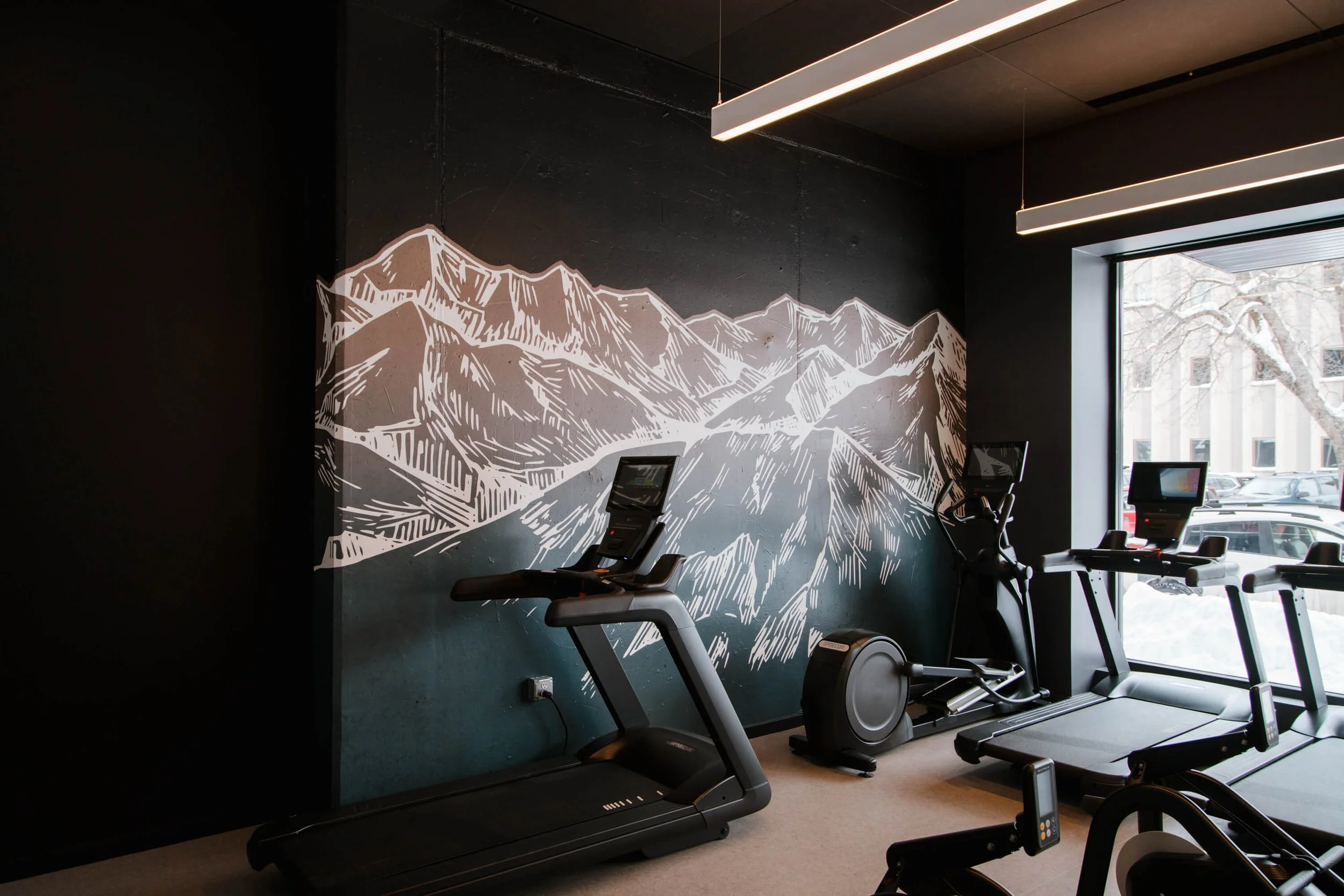 Modern gym interior with a mountain-themed wall wrap in grayscale line art, creating a natural and motivational backdrop for treadmills and fitness equipment in Bozeman, MT.