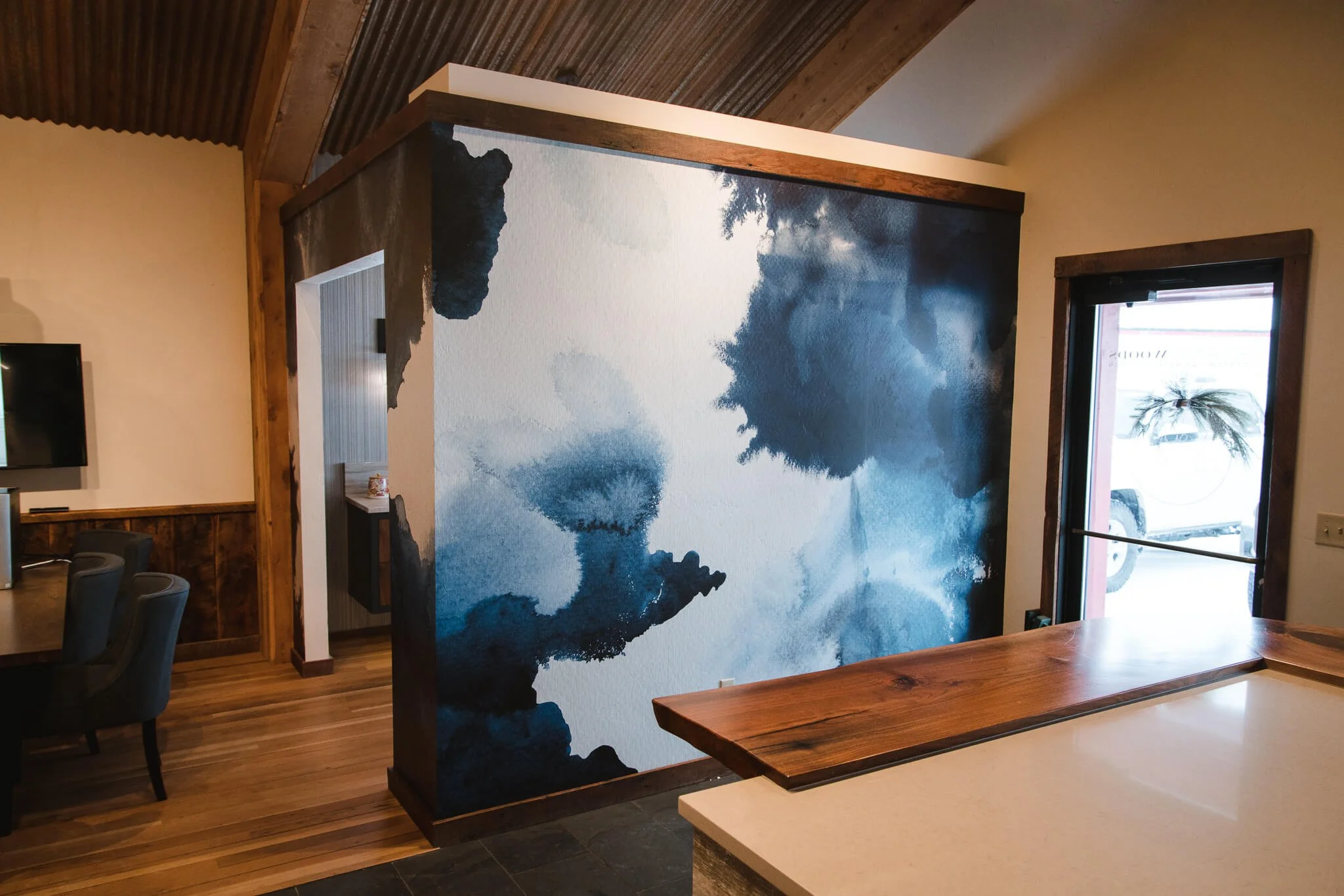 Wall wrap featuring abstract navy and cobalt watercolor-style artwork on a textured accent wall in a rustic office reception area with natural wood and corrugated metal ceiling. Installed by The Wrap Agency at Homestead Woods.