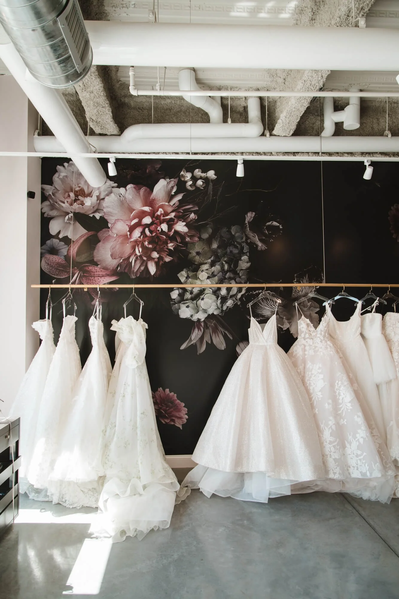 Detailed floral wall wrap featuring oversized pink, white, and maroon blooms as a stylish backdrop to white wedding dresses on display. Installed at The White Dress in Bozeman, MT.