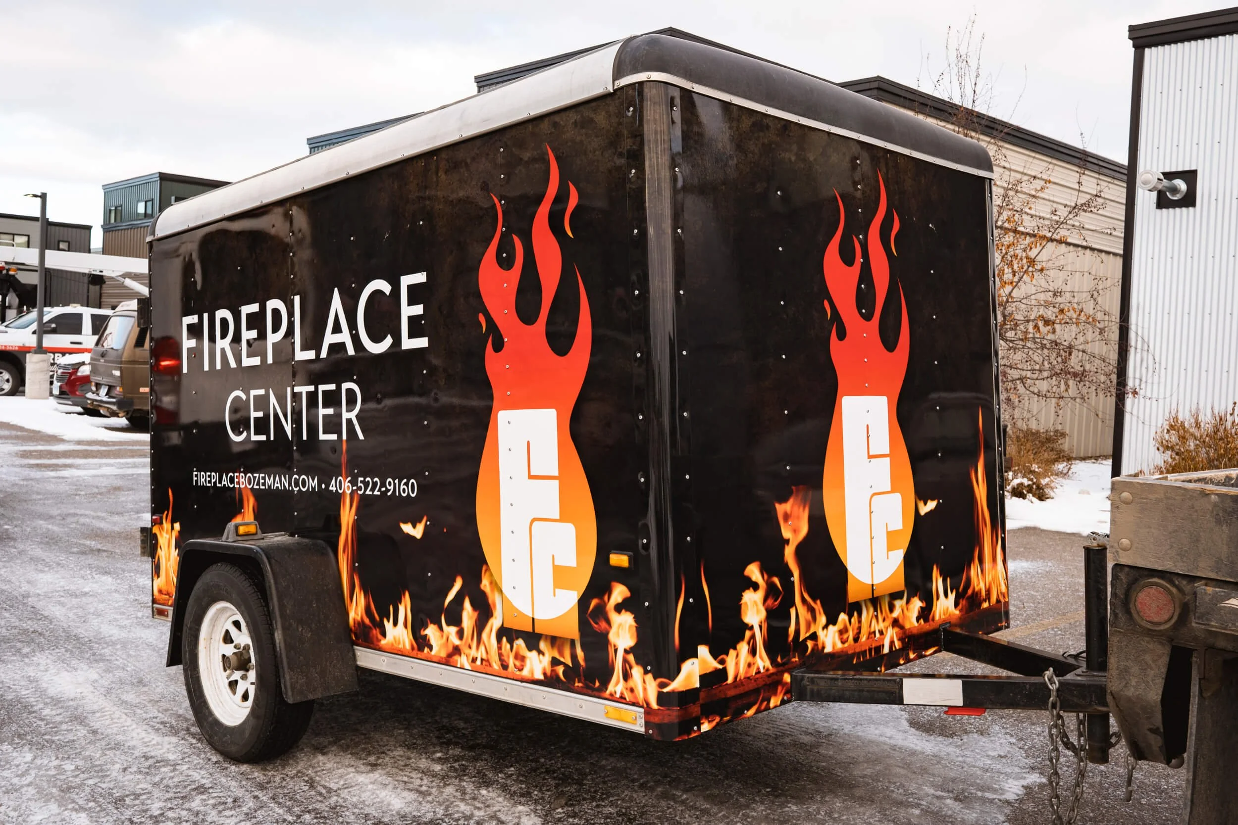 Angled view of the front and side of small trailer with a full trailer wrap with large logos and flames along the bottom
