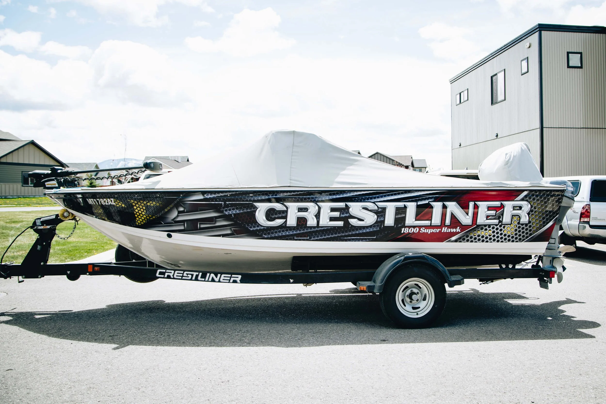 Custom vinyl wrap on a Crestliner fishing boat featuring bold red, black, and silver graphics, viewed from the side and parked outside a commercial building in Bozeman, MT.